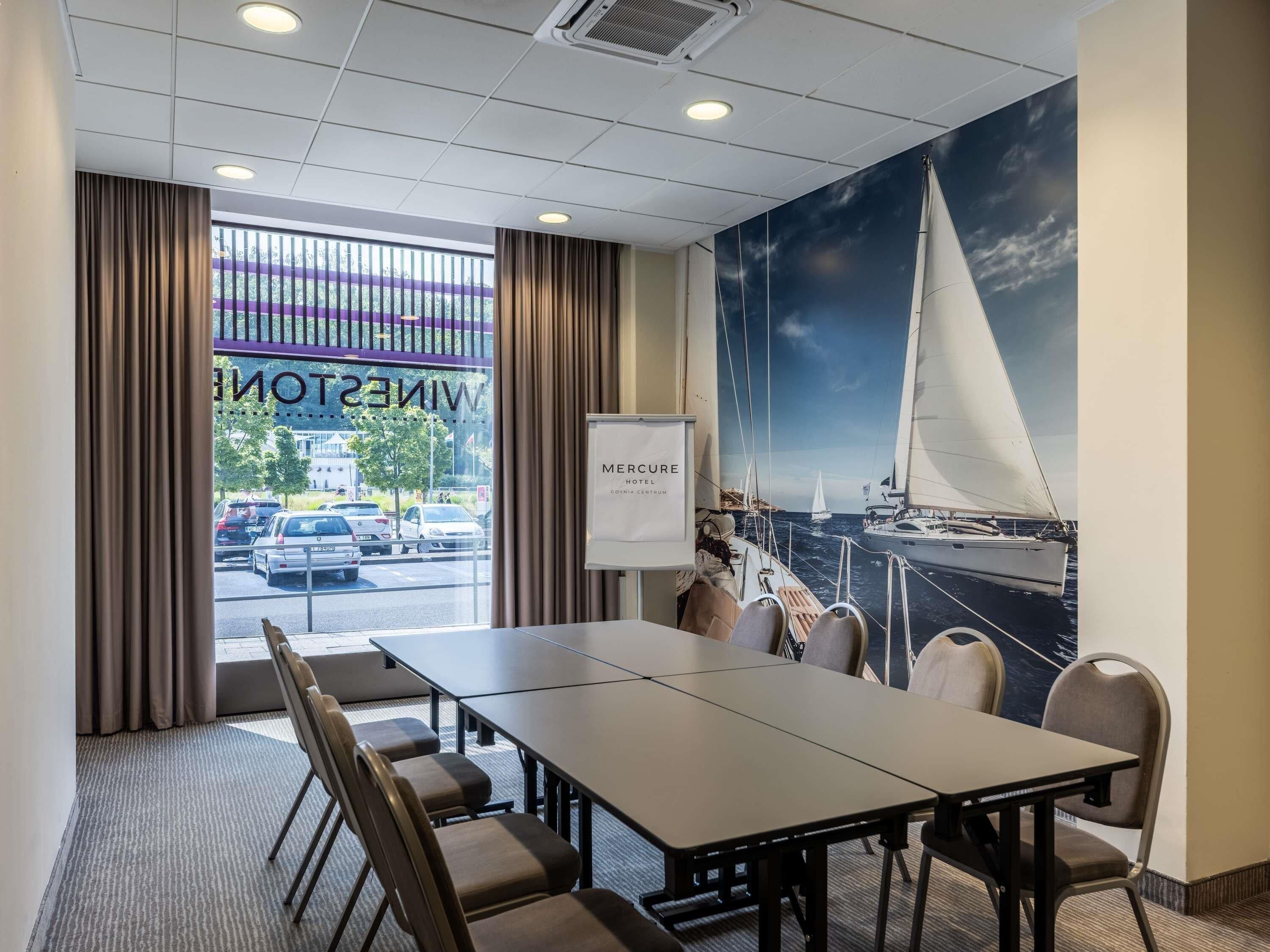 A conference room with a large table, chairs, a view of the street, and a sailboat mural on the wall.