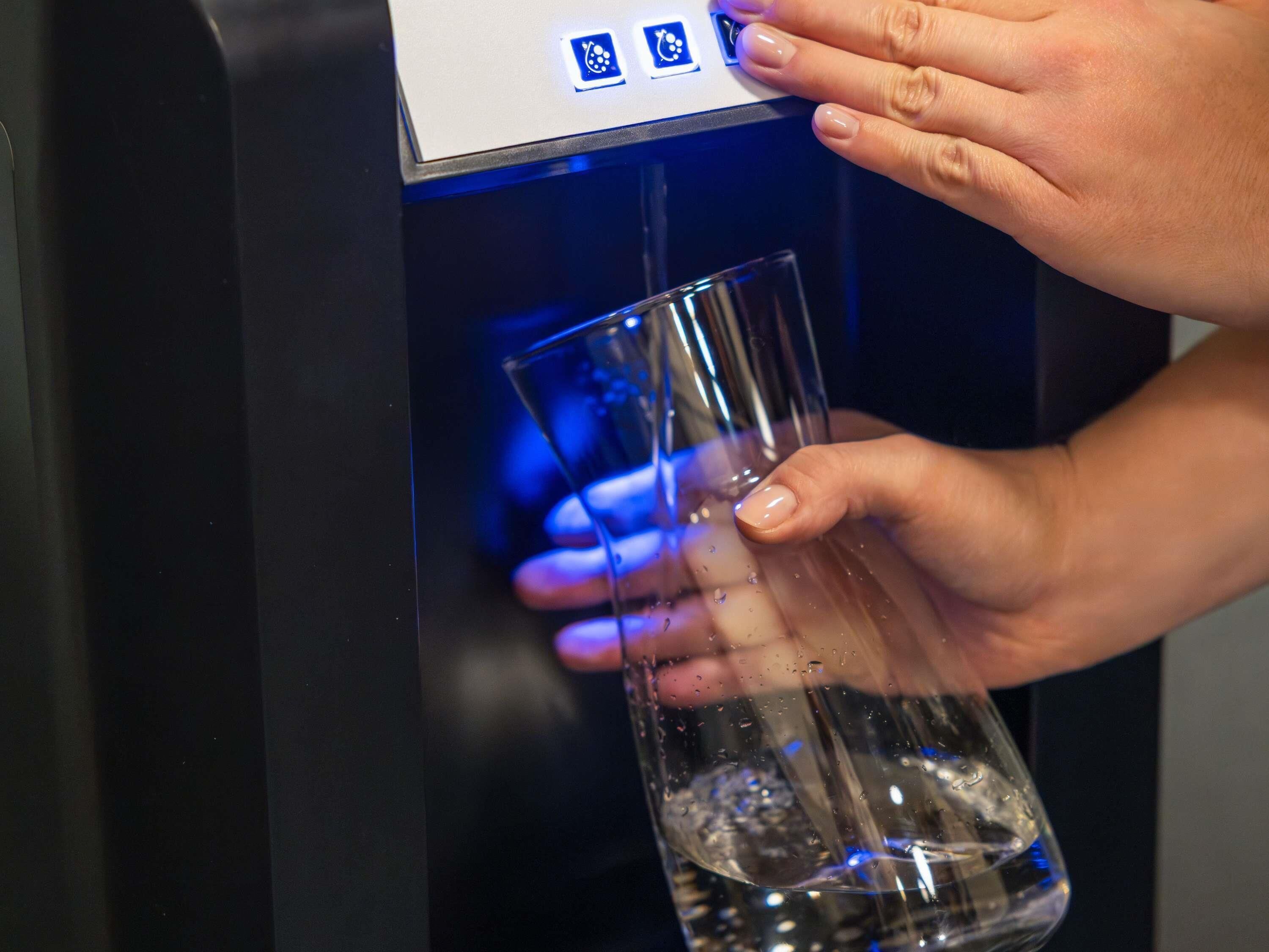 A person using a water dispenser to fill a glass.