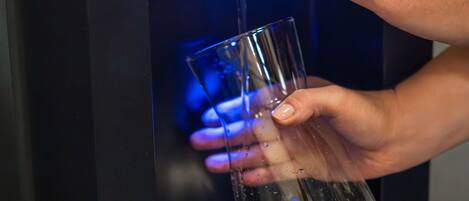 A person using a water dispenser to fill a glass.
