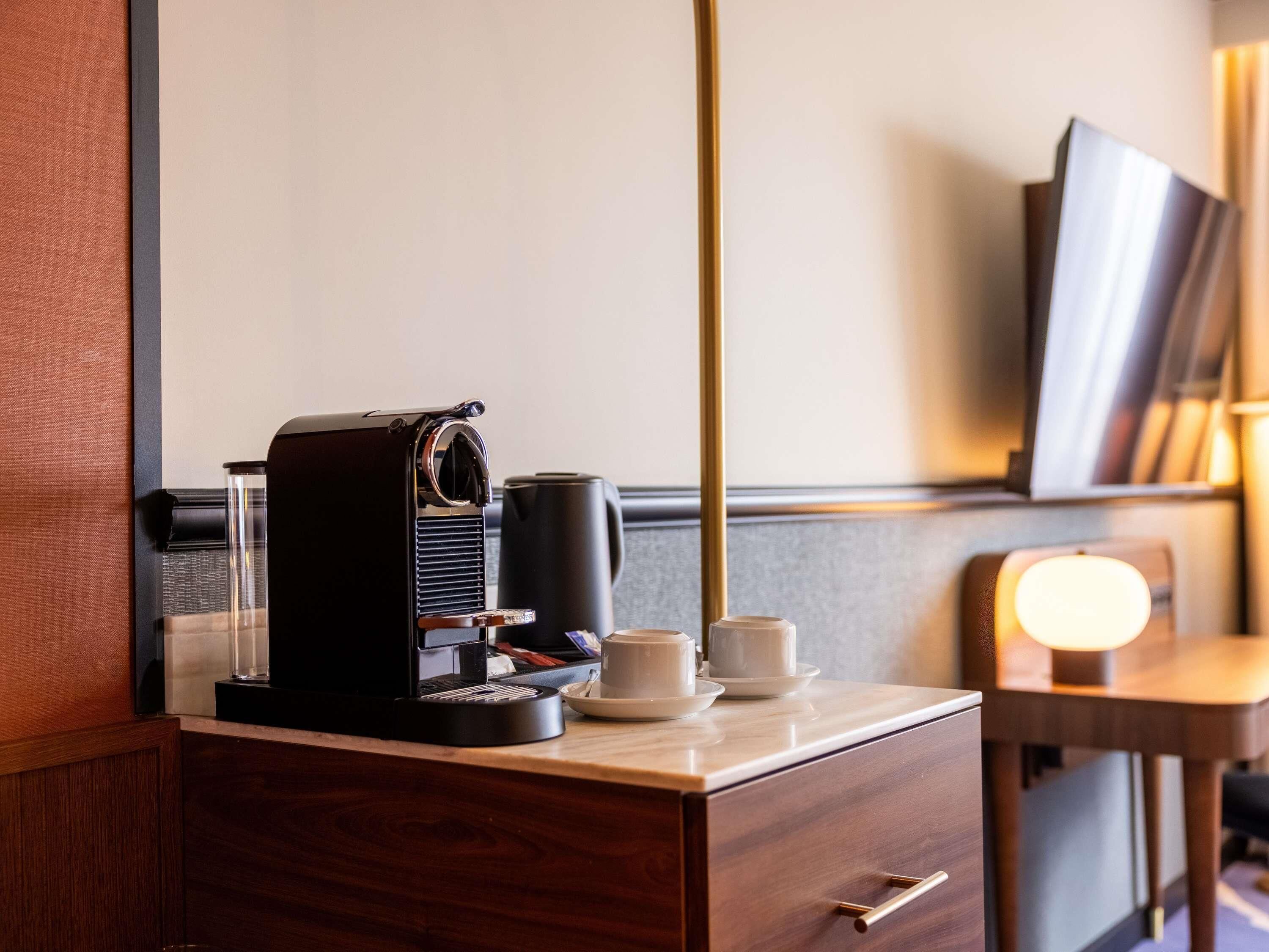 Una habitación de hotel con una cafetera, una taza y un plato sobre un tocador de madera.