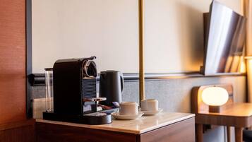 Una habitación de hotel con una cafetera, una taza y un plato sobre un tocador de madera.