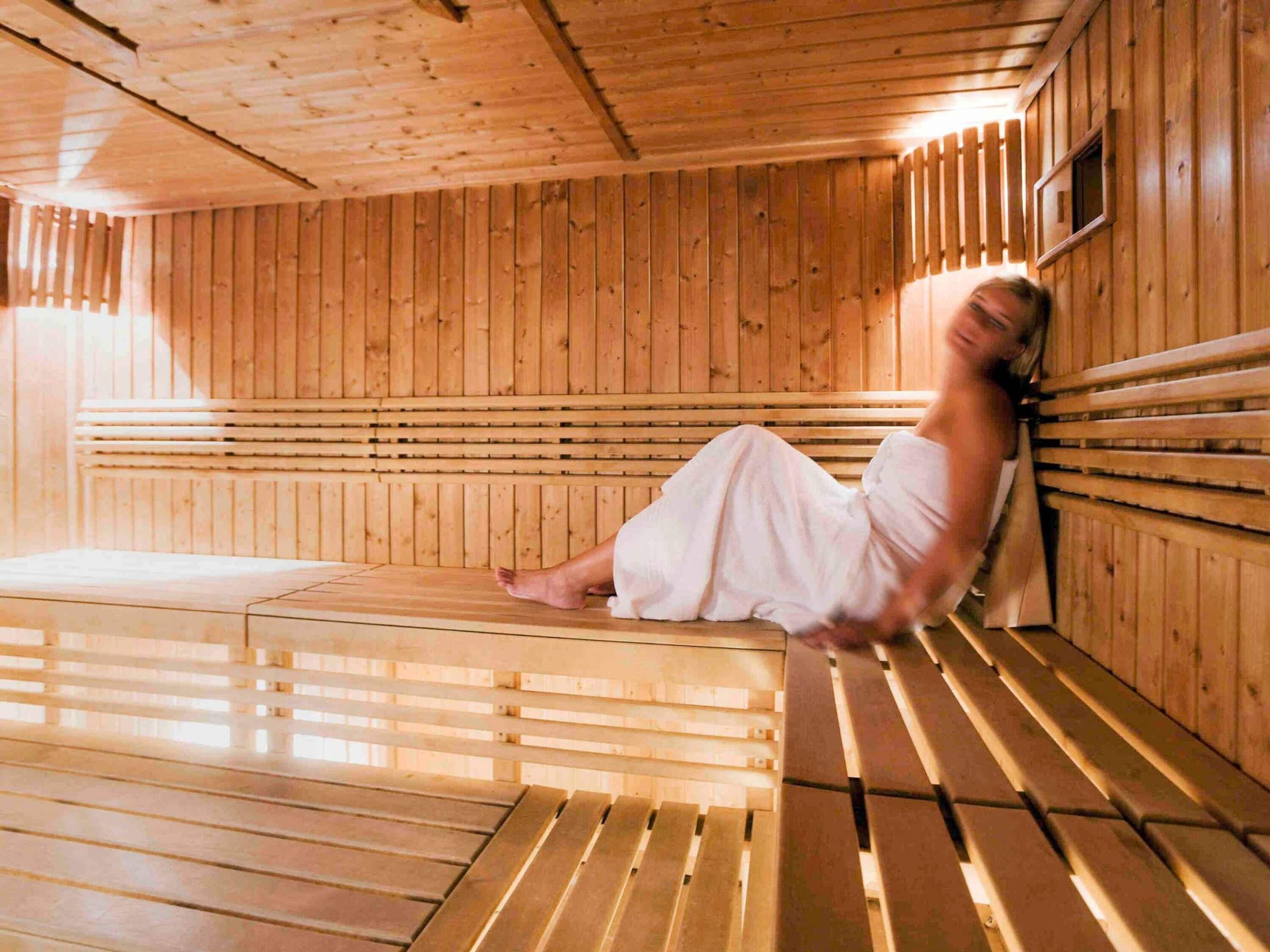 A sauna room with wooden benches and a person sitting on one.