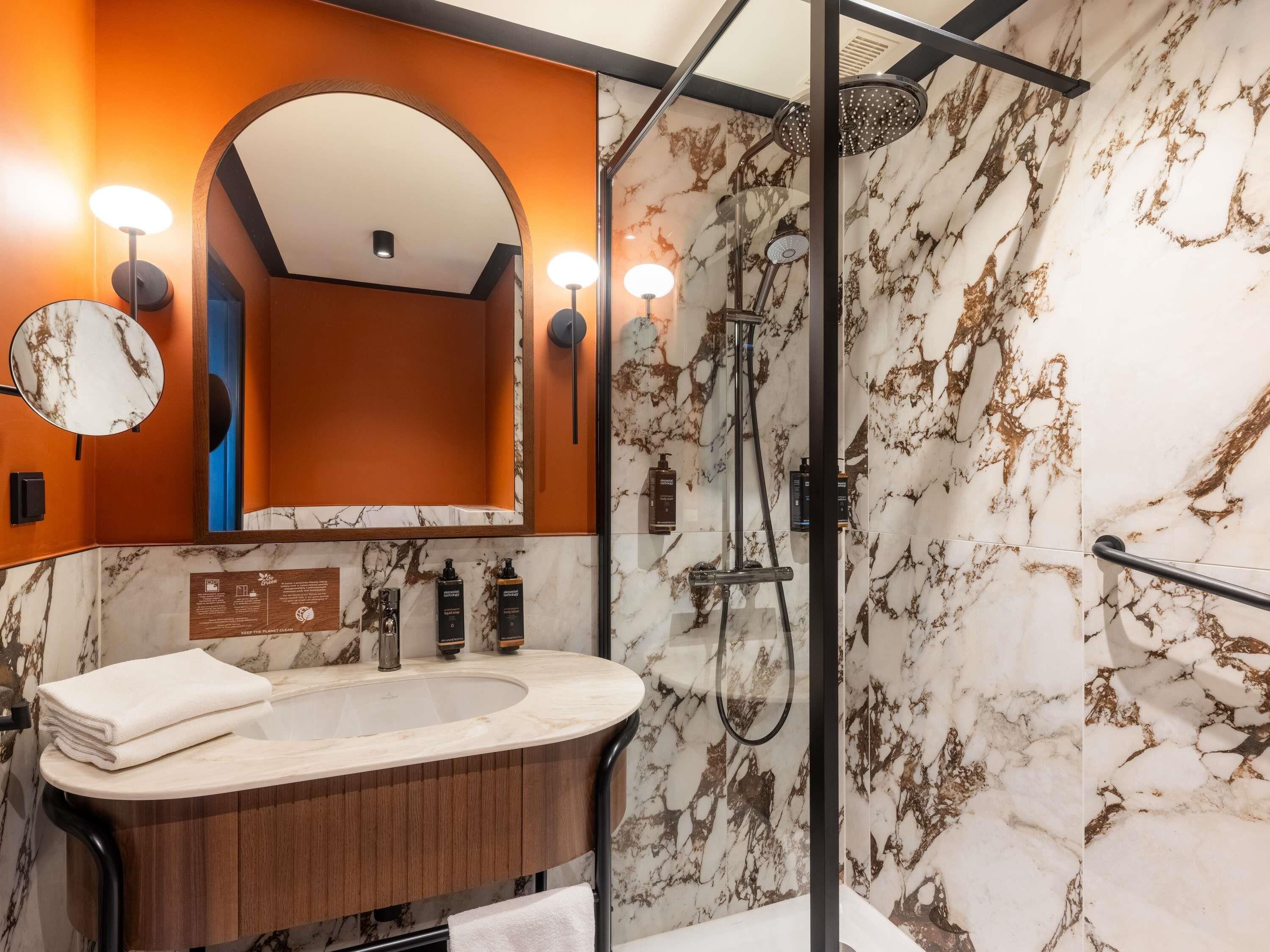 Een badkamer met een marmeren wastafel, een douche met een handdouche en een spiegel met verlichting.