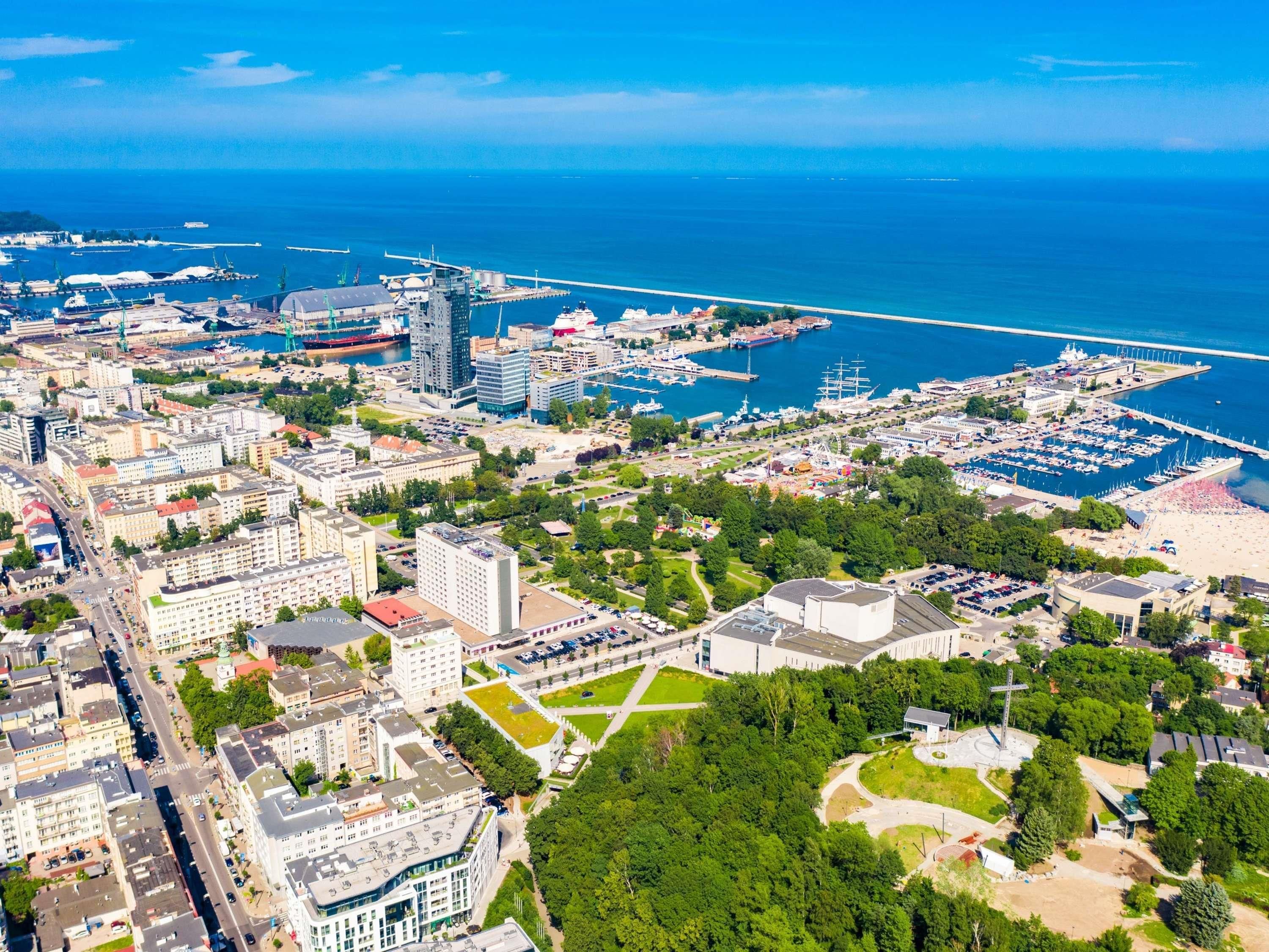 An aerial view of a coastal city with a marina, buildings, and green spaces.