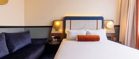 Habitación de hotel con cama, sofá, dos lámparas de noche y una mesita con un vaso.