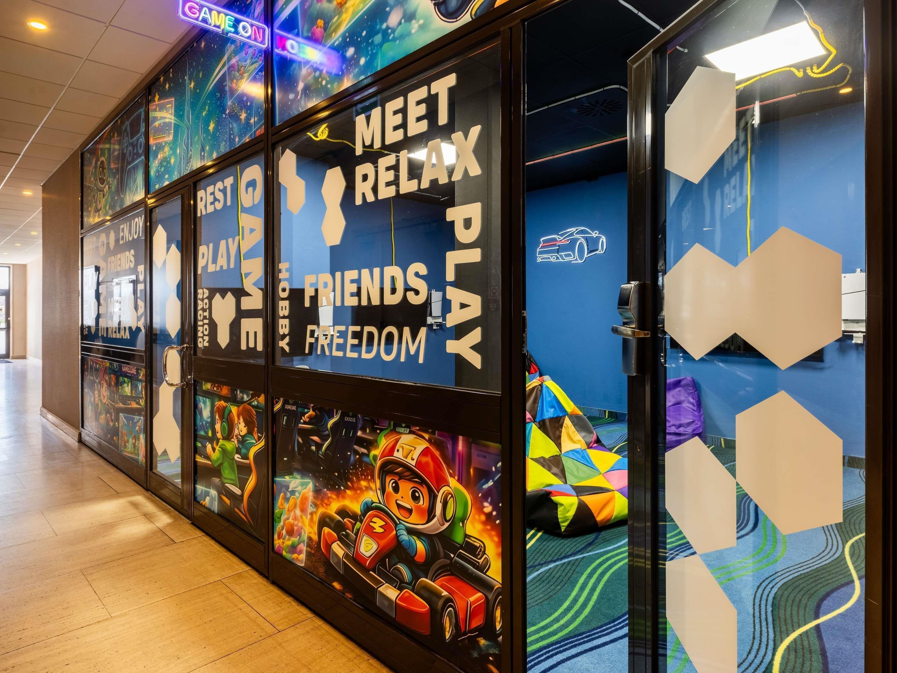 Un couloir orné de bornes d’arcade, de néons et d’un mur bleu orné de motifs hexagonaux.