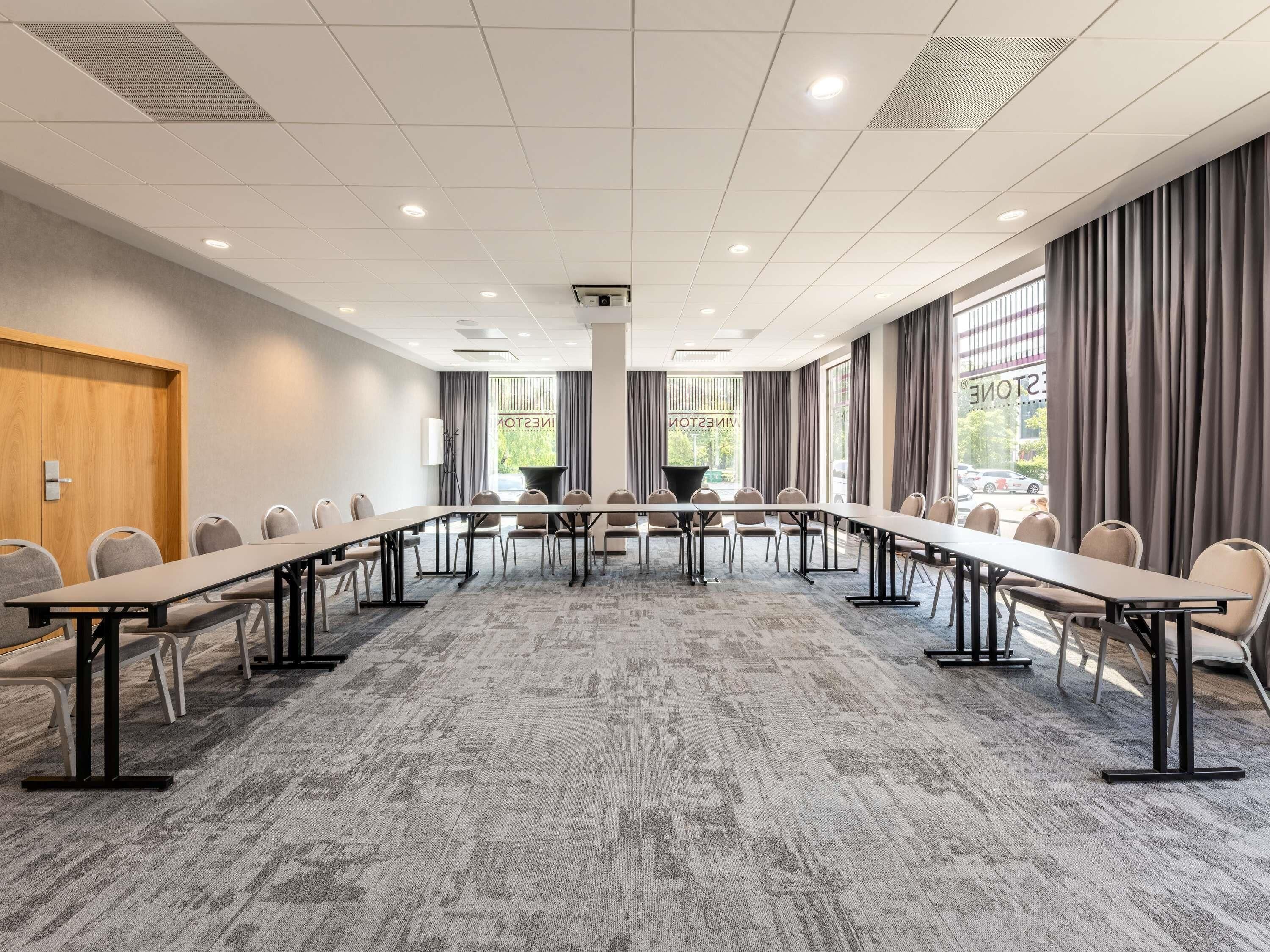A conference room with a long table, chairs, a projector, and large windows with curtains.