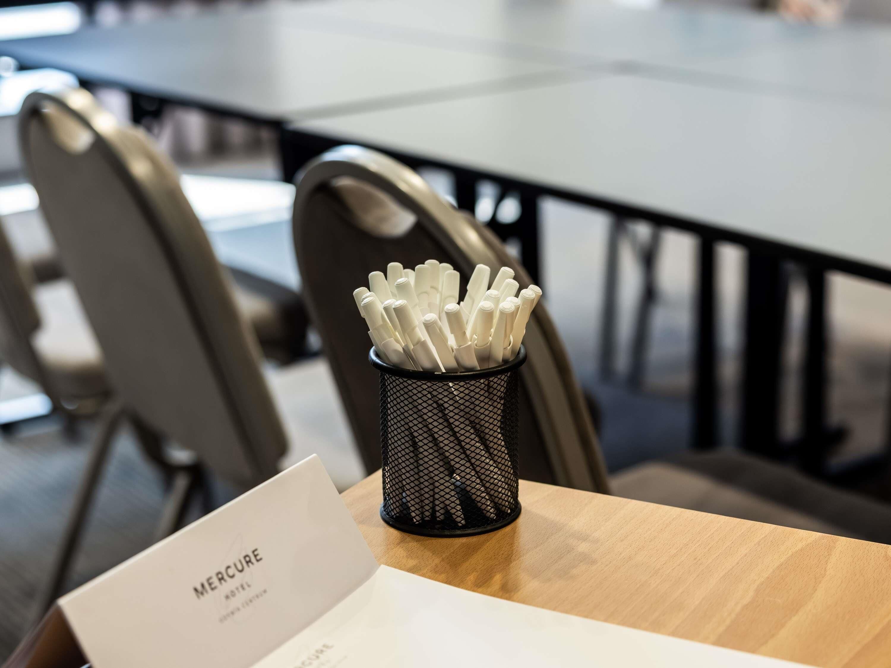 A hotel room with a wooden table, a black mesh pen holder with white pens, and a sign reading 'Mercure Hotel.'