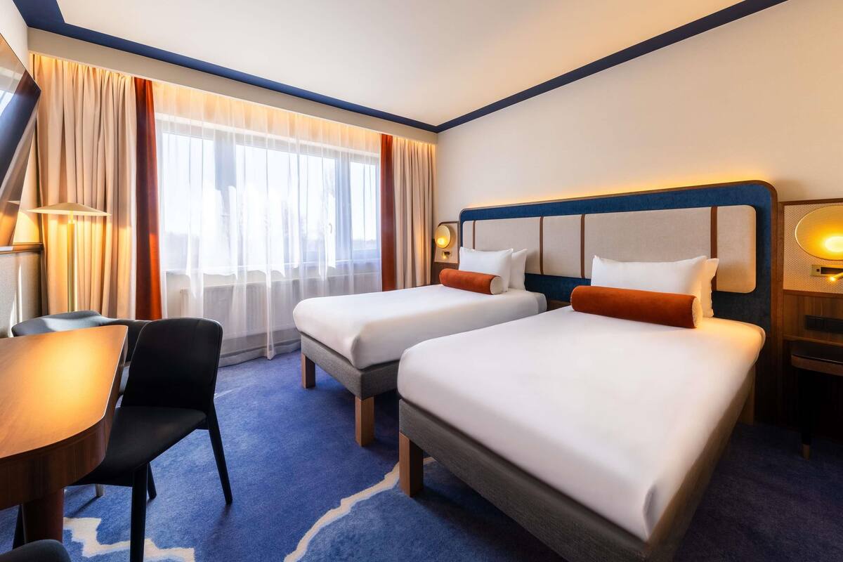 A hotel room with two beds, a desk, and a chair.
