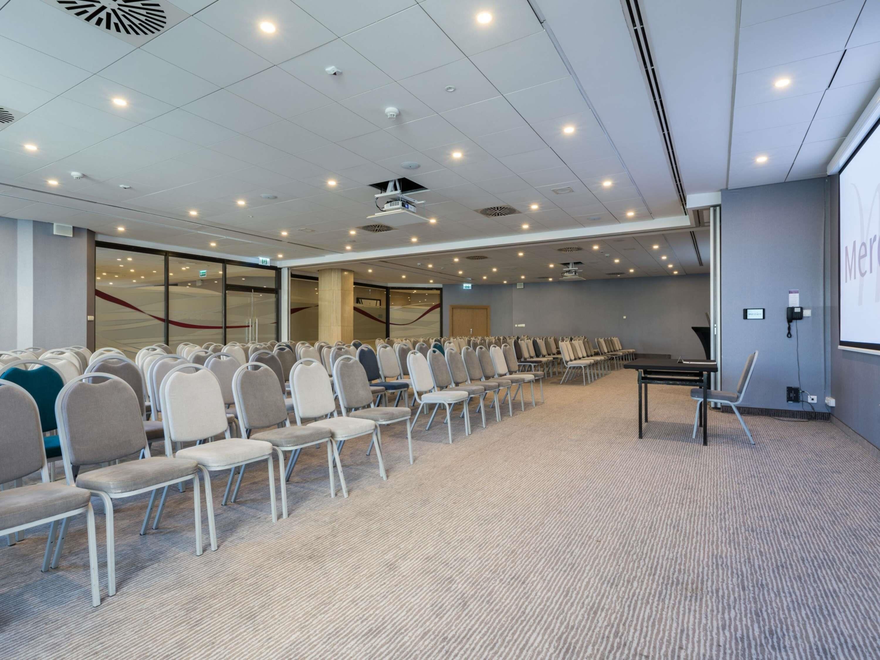 A conference room with rows of chairs, a projector screen, and a carpeted floor.