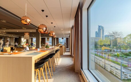Un restaurante moderno con una barra alargada, taburetes y amplios ventanales con vista a la ciudad.