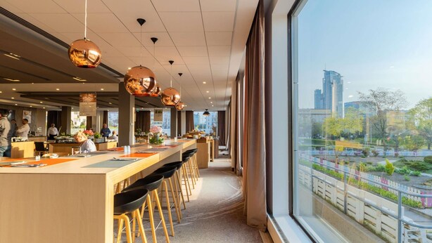 Un restaurant moderne doté d’un long comptoir, de tabourets de bar et de grandes fenêtres offrant une vue sur la ville.