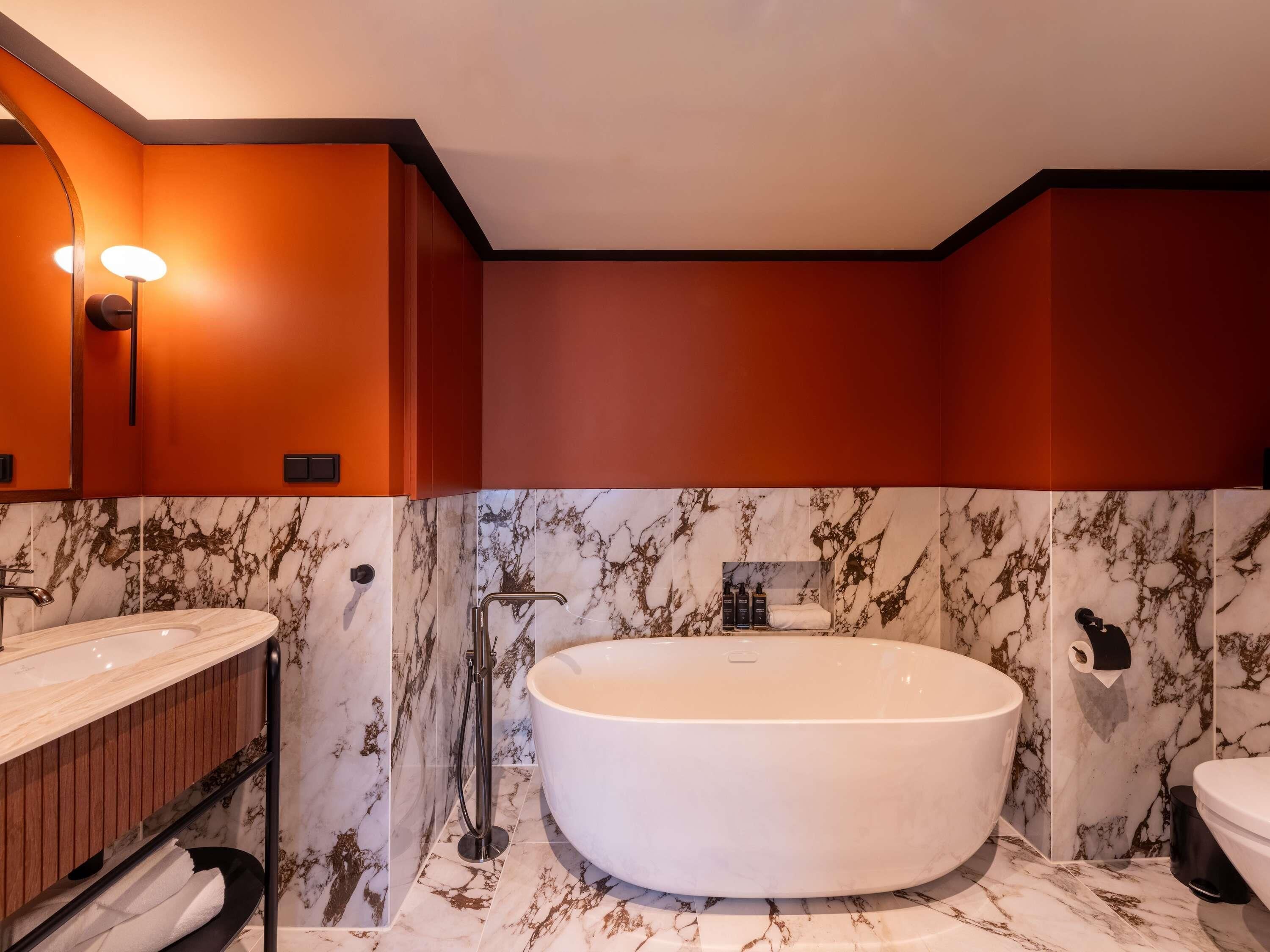 A modern bathroom with a freestanding bathtub, a vanity with a mirror, and marble-patterned walls.