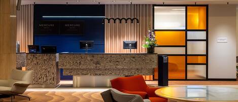 A hotel reception area with a modern design, featuring a reception desk, seating area, and a decorative plant.