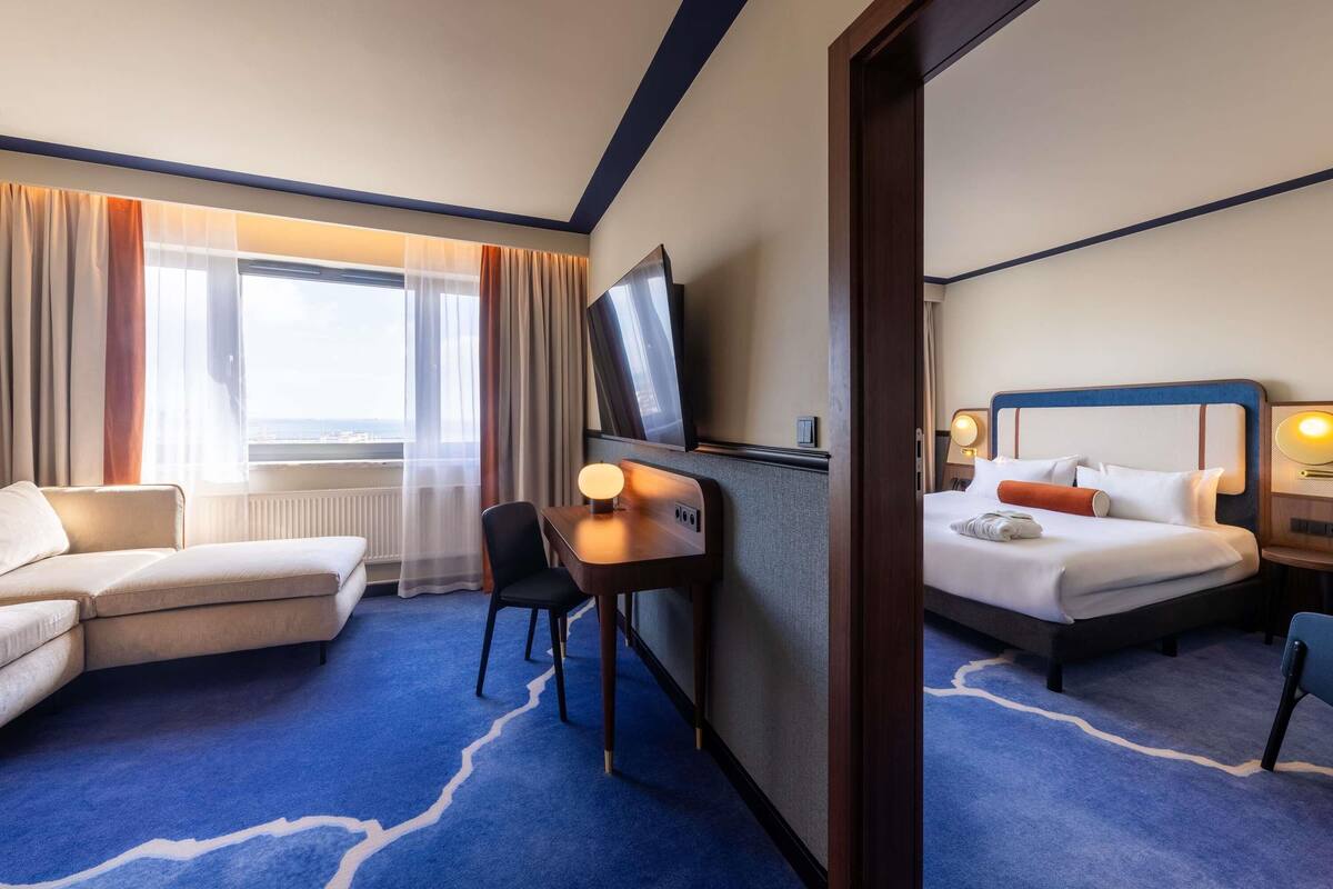 A hotel room with a bed, a desk, a chair, a TV, and a view of the city.