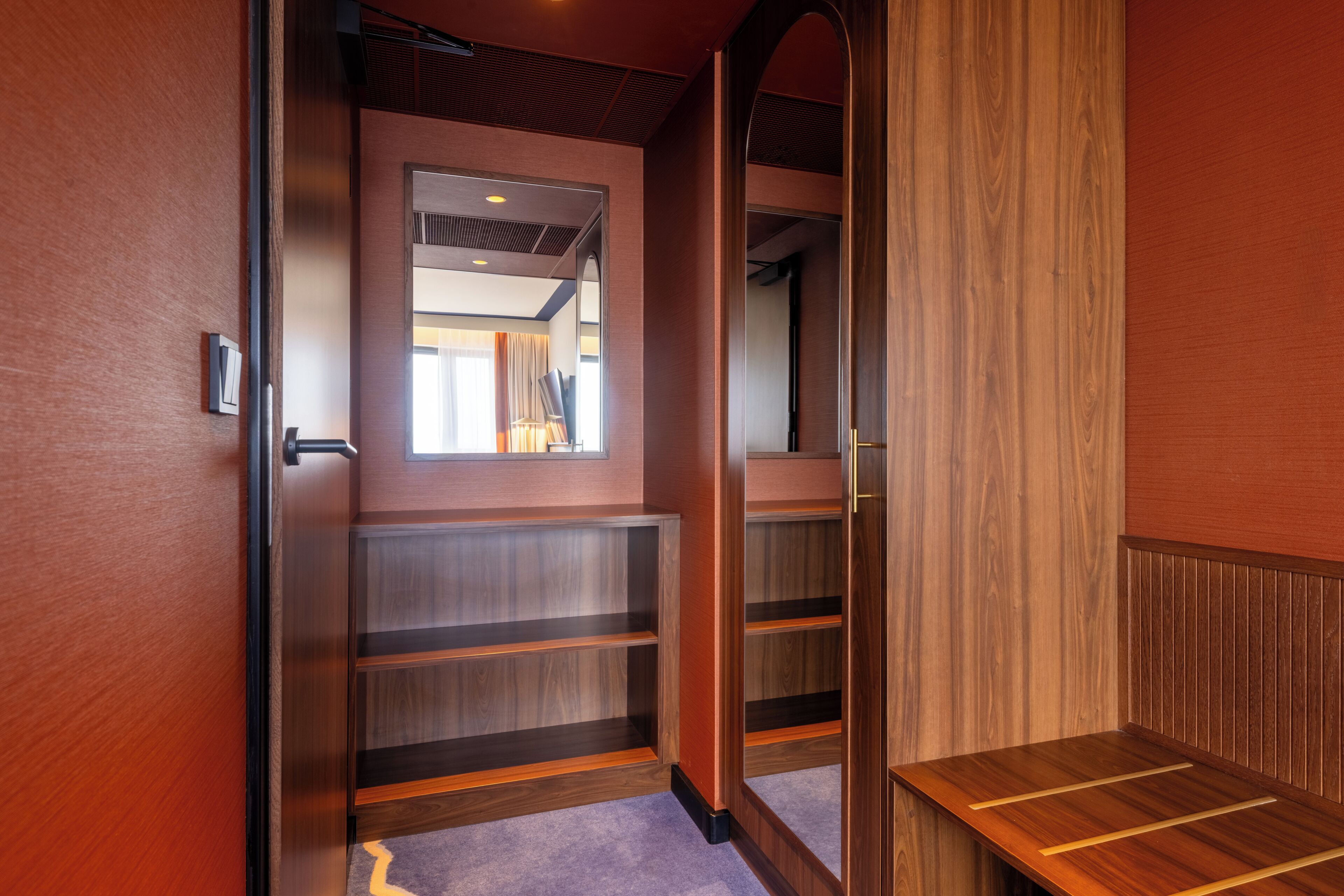 Un pasillo con estanterías de madera, un espejo y una puerta que da a otra habitación.