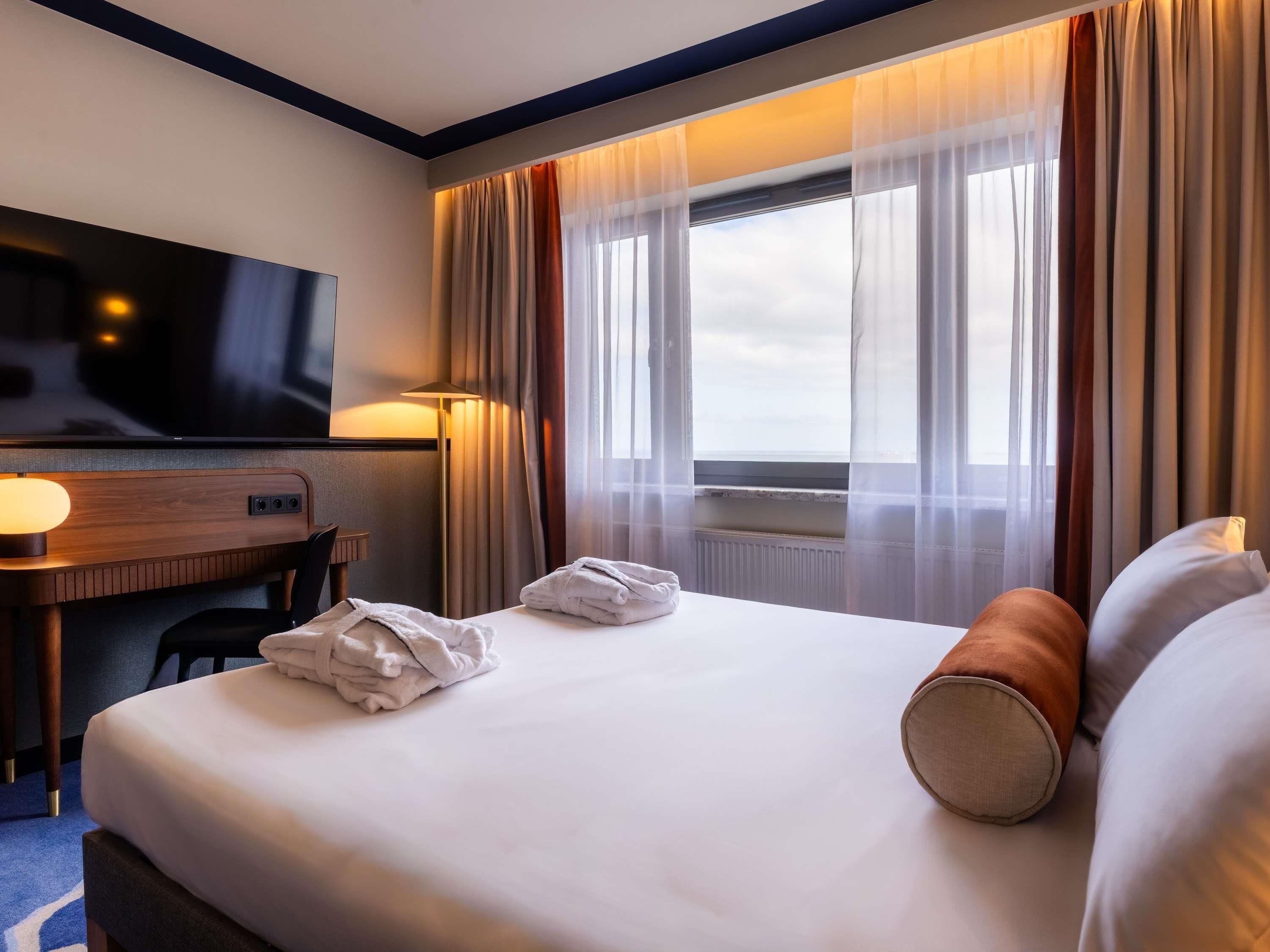 A hotel room with a bed, a desk, a television, and a window with curtains.