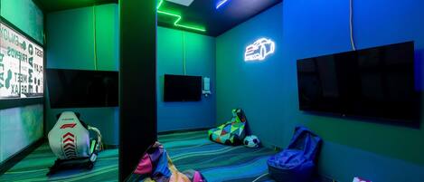 Una habitación con un sillón de mezcla colorido, un asiento de carreras, un letrero de coche con luces de neón y un televisor en la pared.