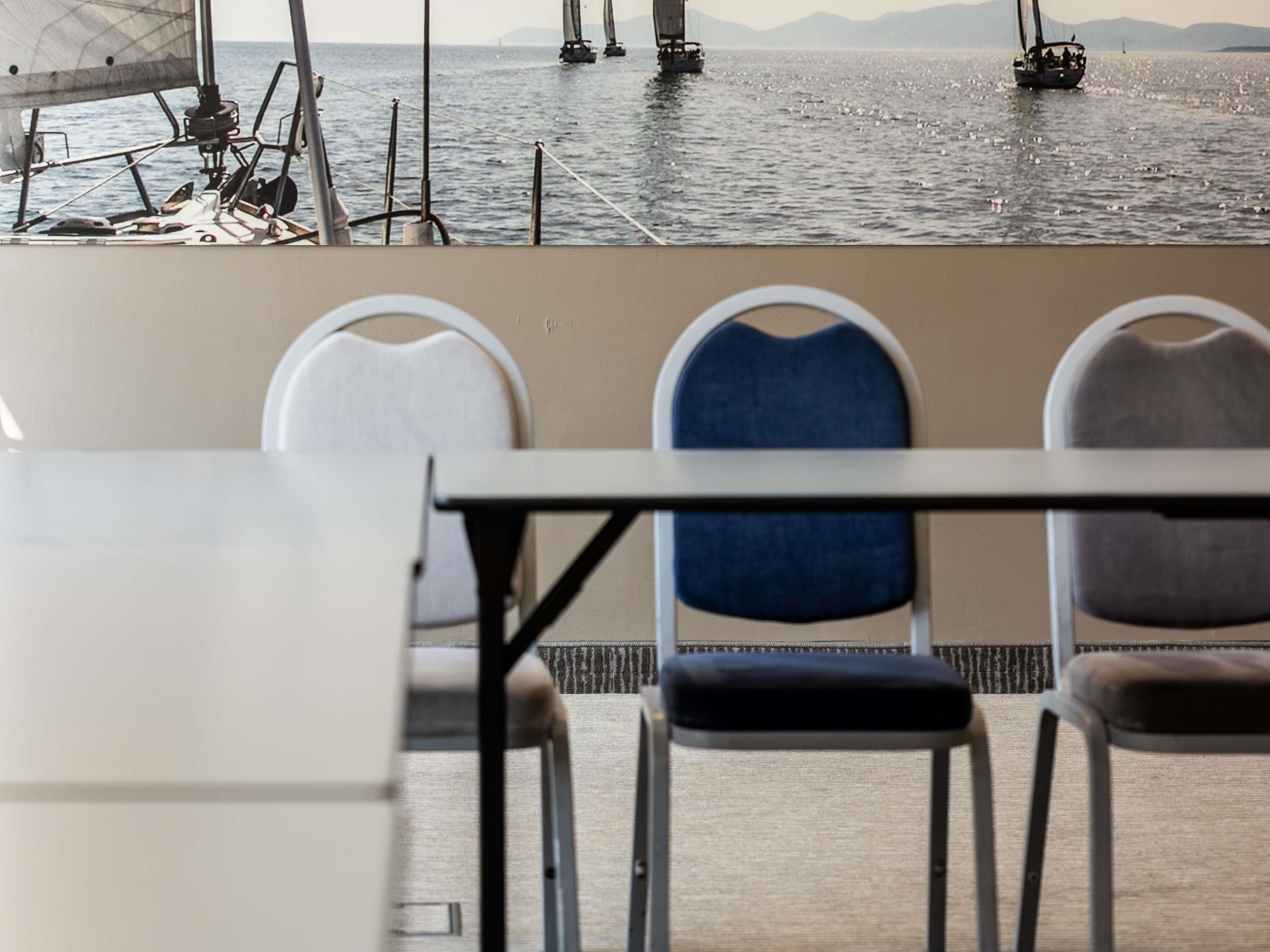 Une vue sur un coin repas avec une table et des chaises, donnant sur une étendue d’eau calme où voguent des voiliers.