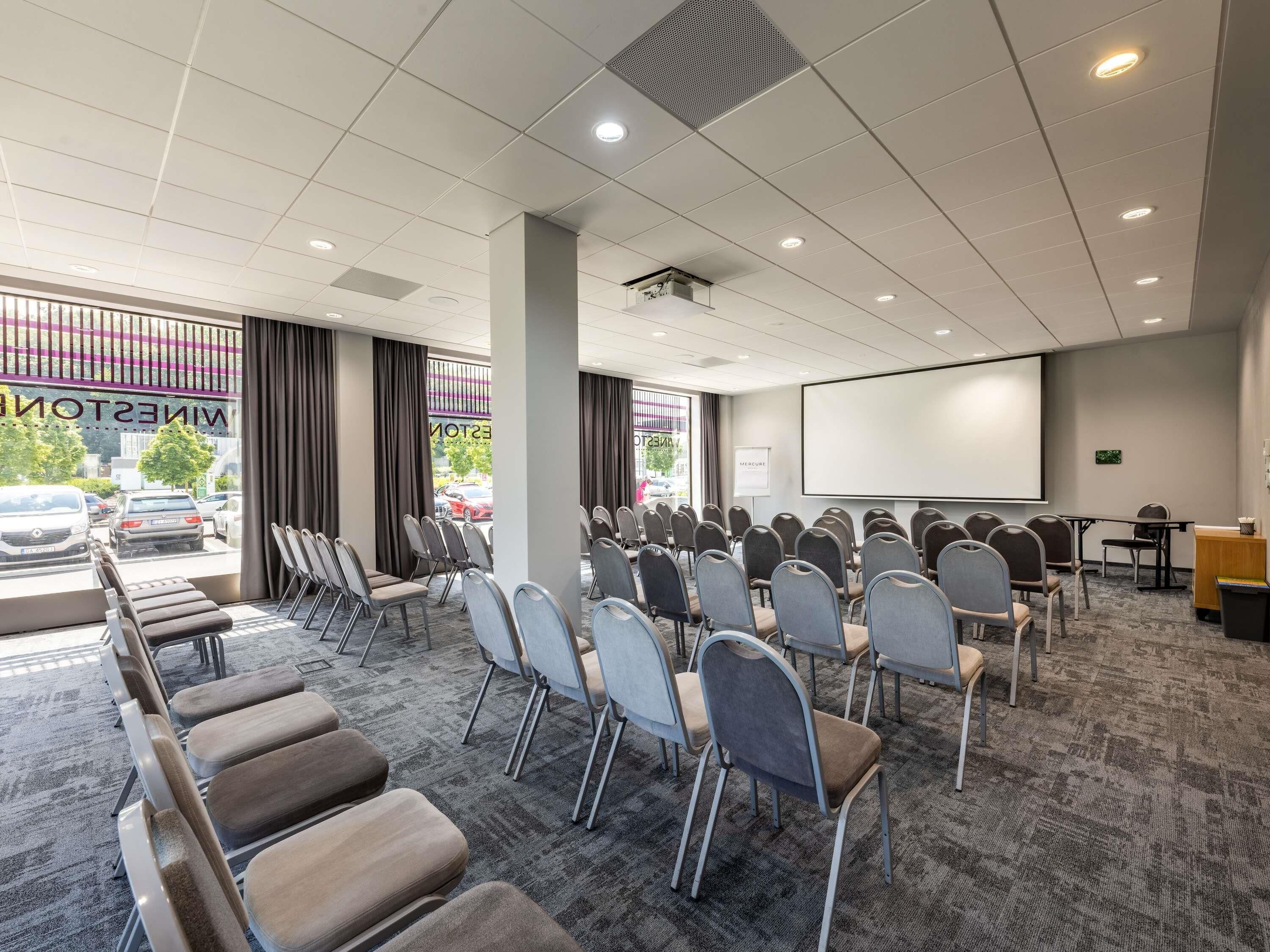 A conference room with rows of chairs, a projector screen, and a carpeted floor.