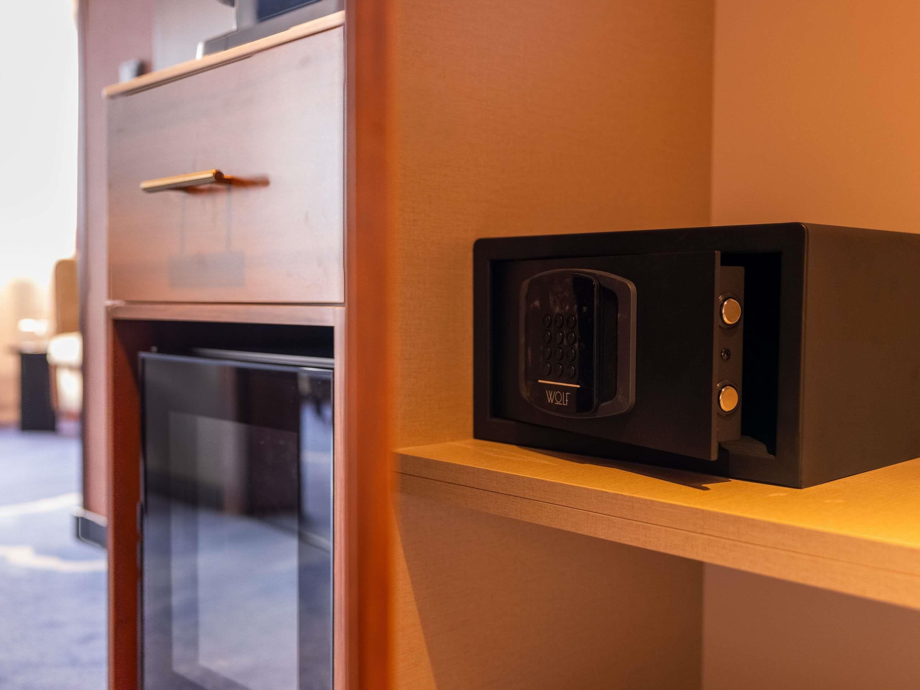 A microwave on a wooden shelf in a kitchen area with a refrigerator below.