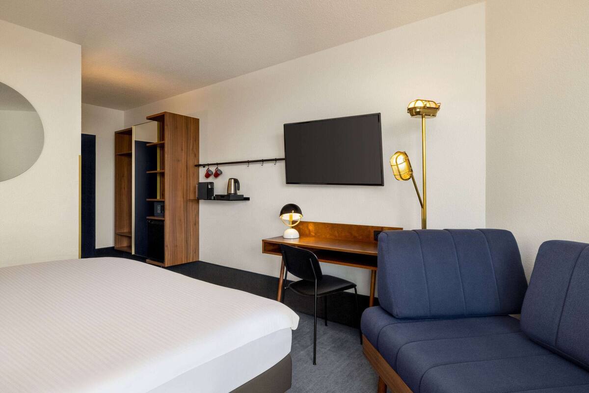 Une chambre d’hôtel comprenant un lit, un bureau avec une chaise, une télévision, une lampe et une armoire.