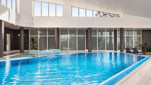 A modern indoor swimming pool with clear glass walls, large windows, and a tiled floor.