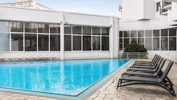 Una piscina amb gandules i una terrassa amb paviment de pedra.