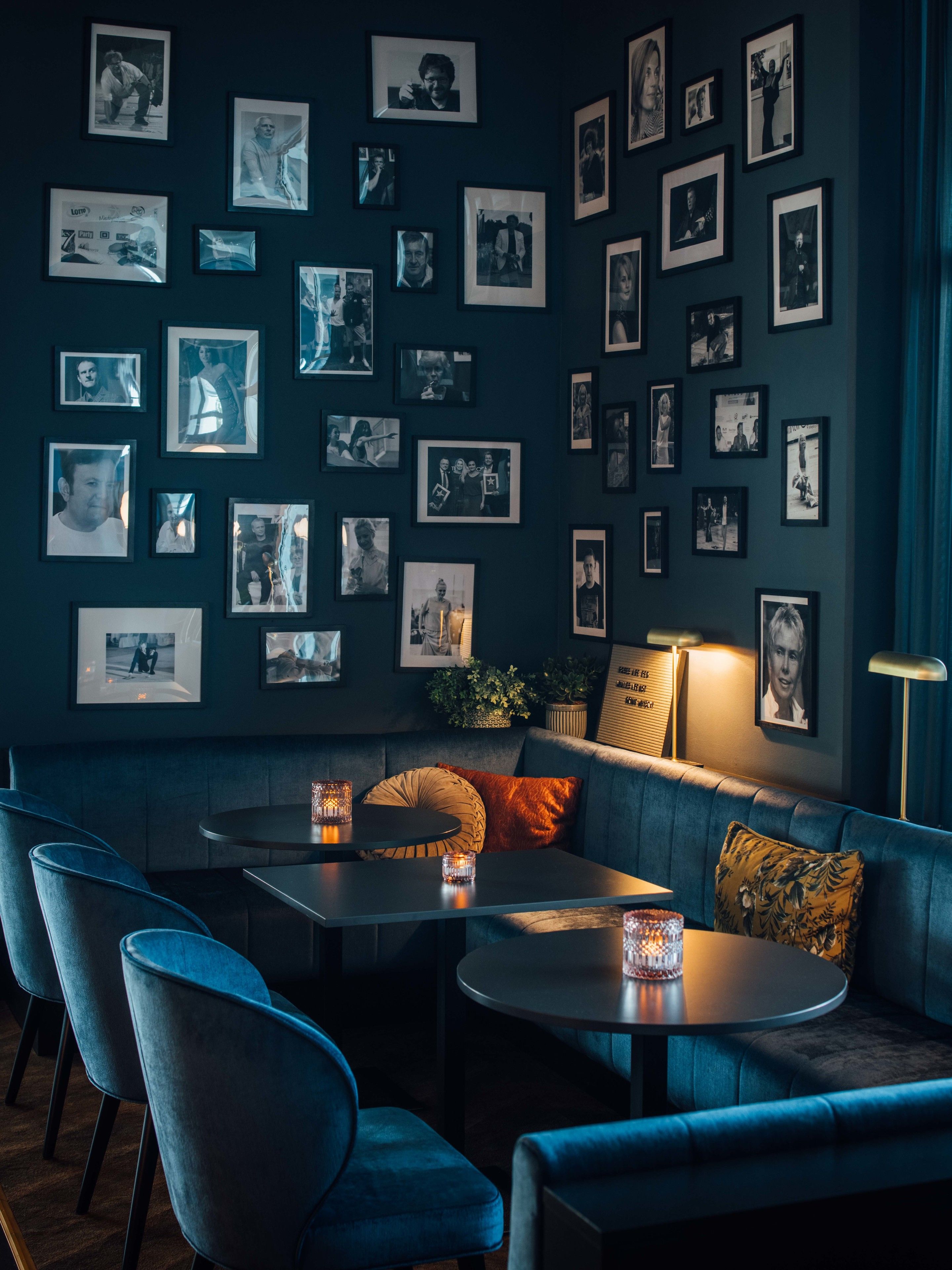 Un salon moderne aux couleurs dominantes bleu foncé, comprenant un canapé, des fauteuils, une table ronde et un mur orné de nombreuses photographies encadrées.