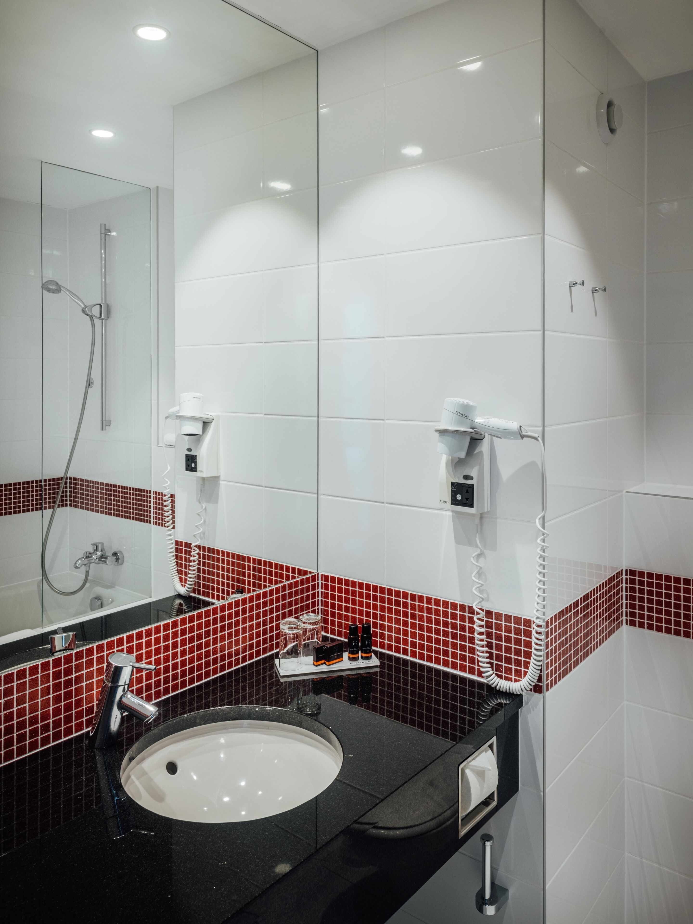 Une salle de bain moderne avec un lavabo blanc, une douche en verre et des éléments décoratifs en carreaux rouges.