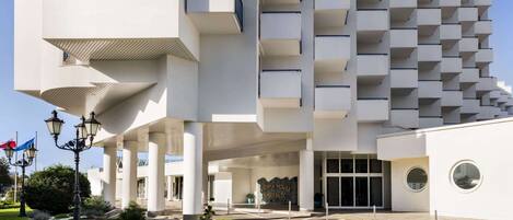 A modern hotel with a unique geometric facade, large balconies, and a well-maintained garden.