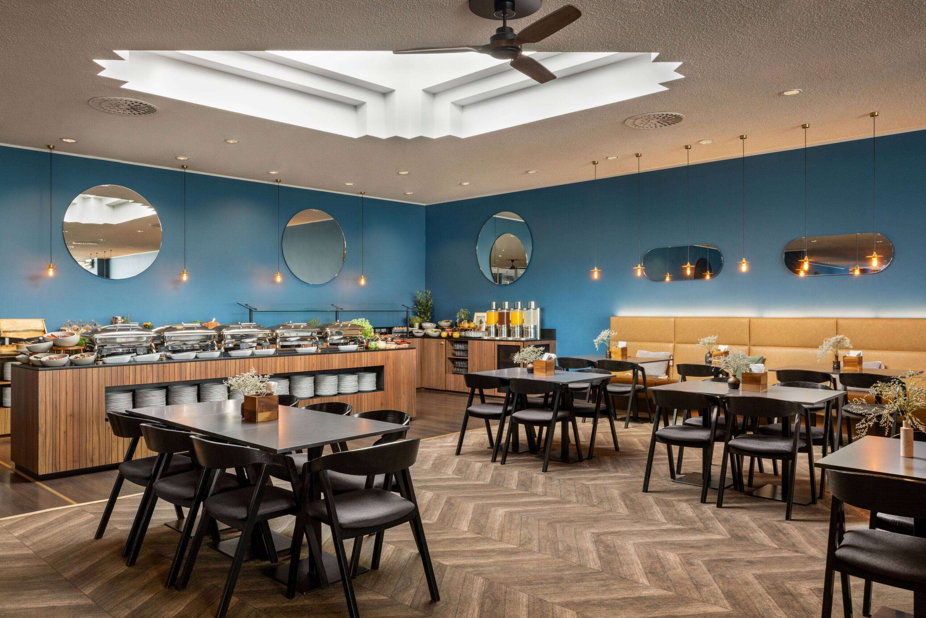 A modern restaurant with a central bar area, multiple dining tables, and a herringbone patterned floor.