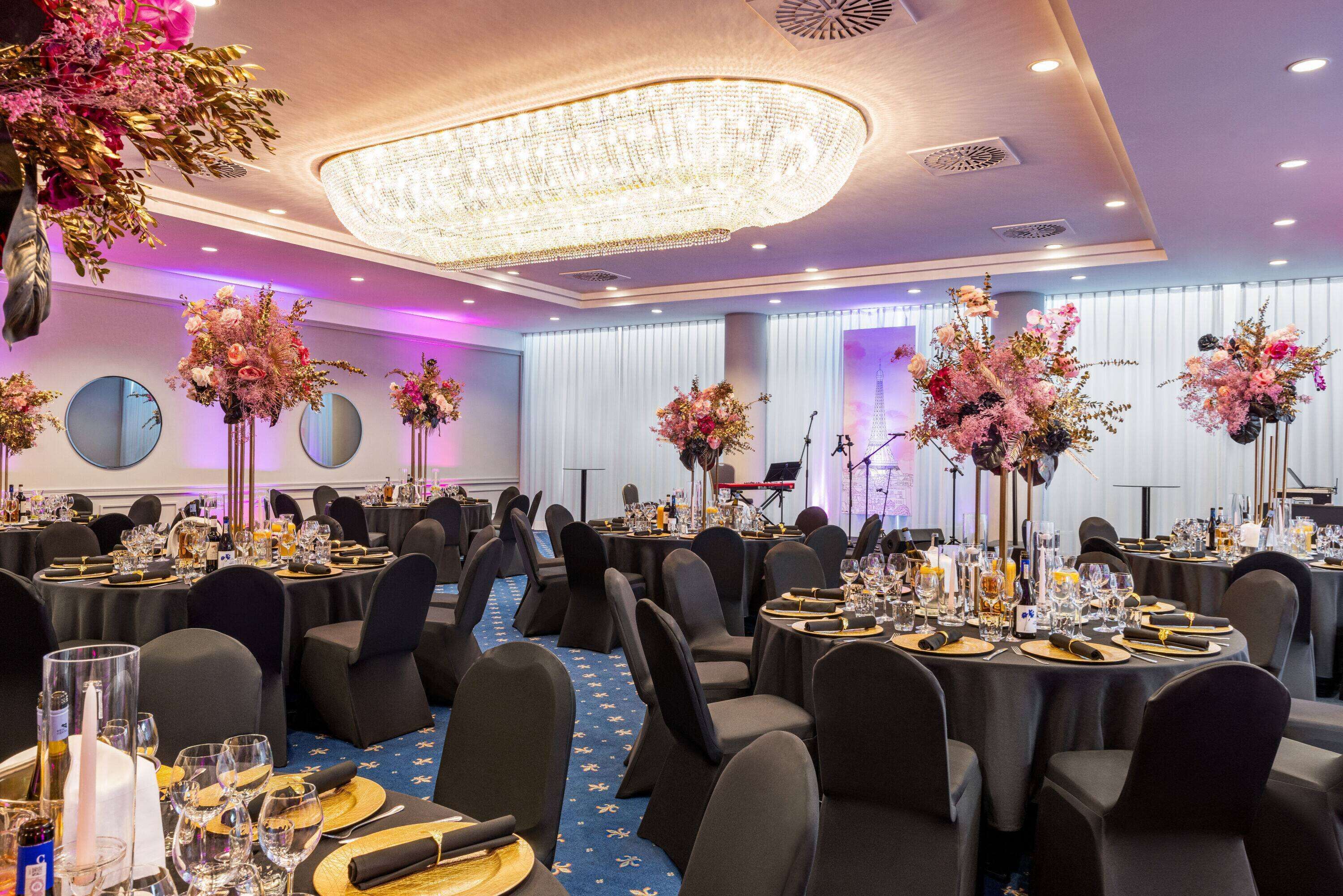 A banquet hall with round tables, black chairs, and floral centerpieces.