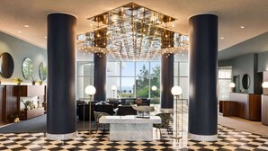 A lobby with a checkered floor, large columns, a central seating area with sofas and a marble table, and a hanging light fixture.