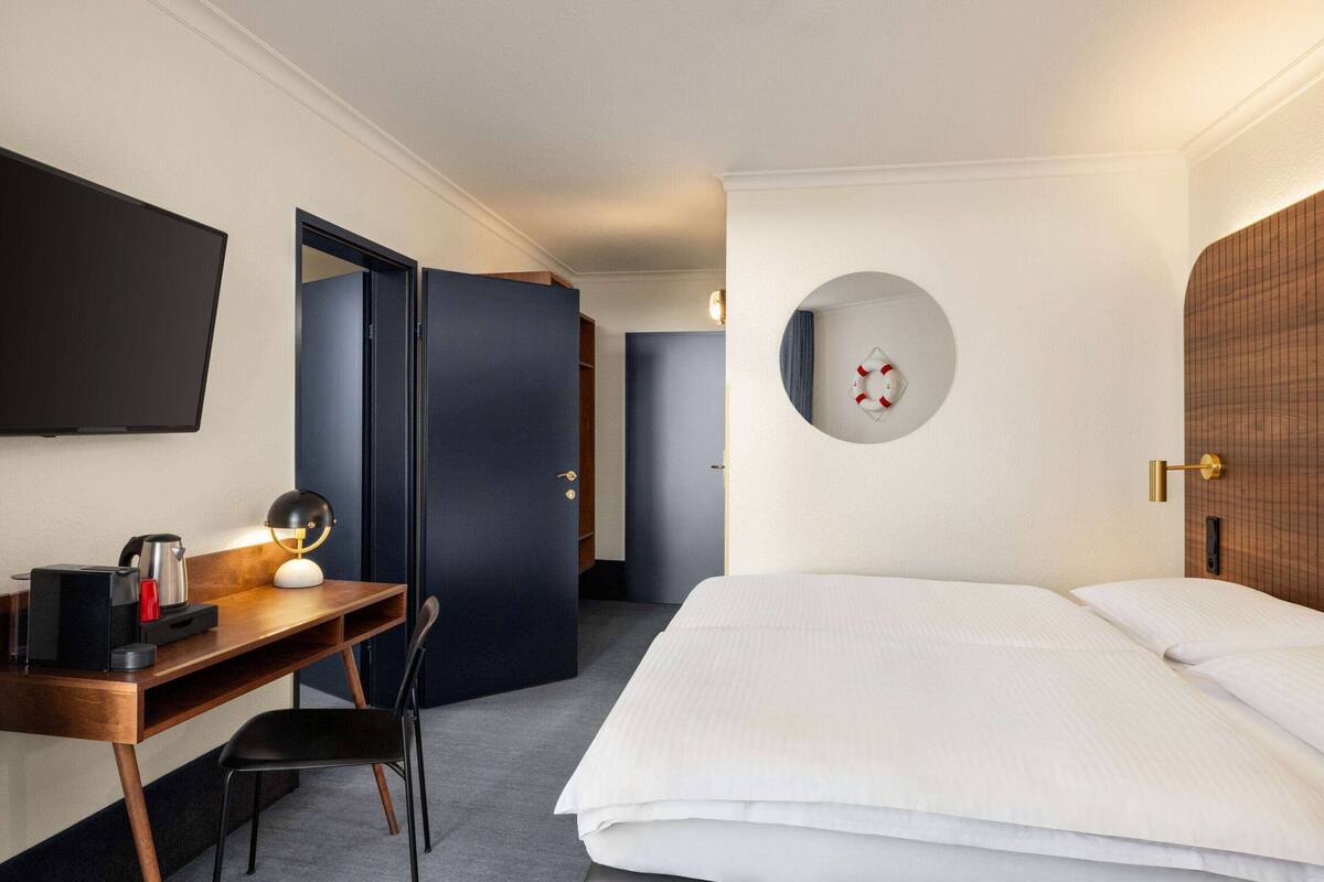 Une chambre d’hôtel avec un lit, un bureau doté d’une lampe, une télévision et un miroir rond accroché au mur.