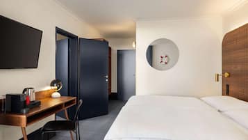 Habitació d'hotel amb llit, escriptori amb làmpada, televisió i un mirall rodó a la paret.
