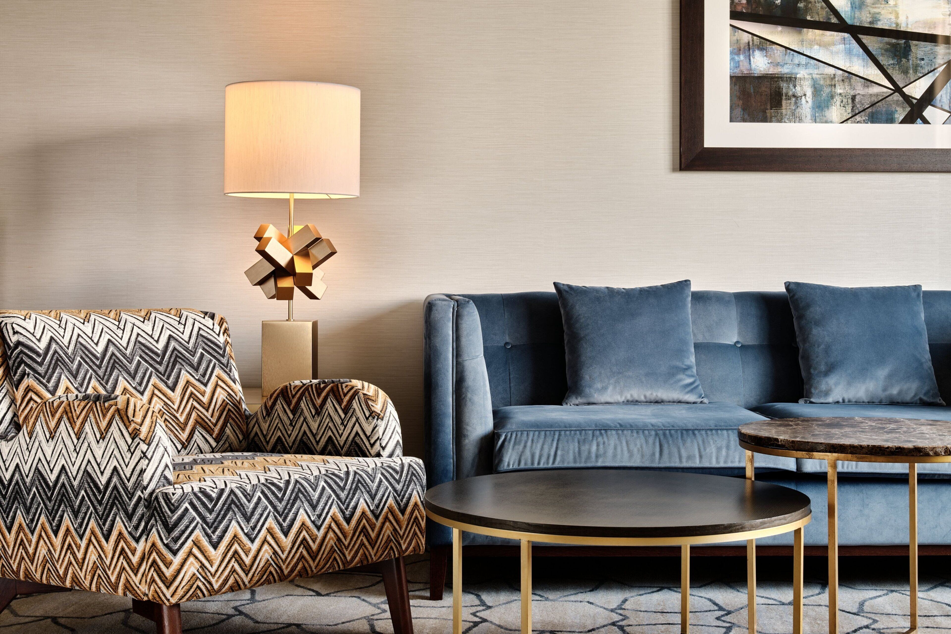 Uma sala de estar moderna com uma poltrona estampada, um sofá azul, uma mesa de centro redonda e um abajur.