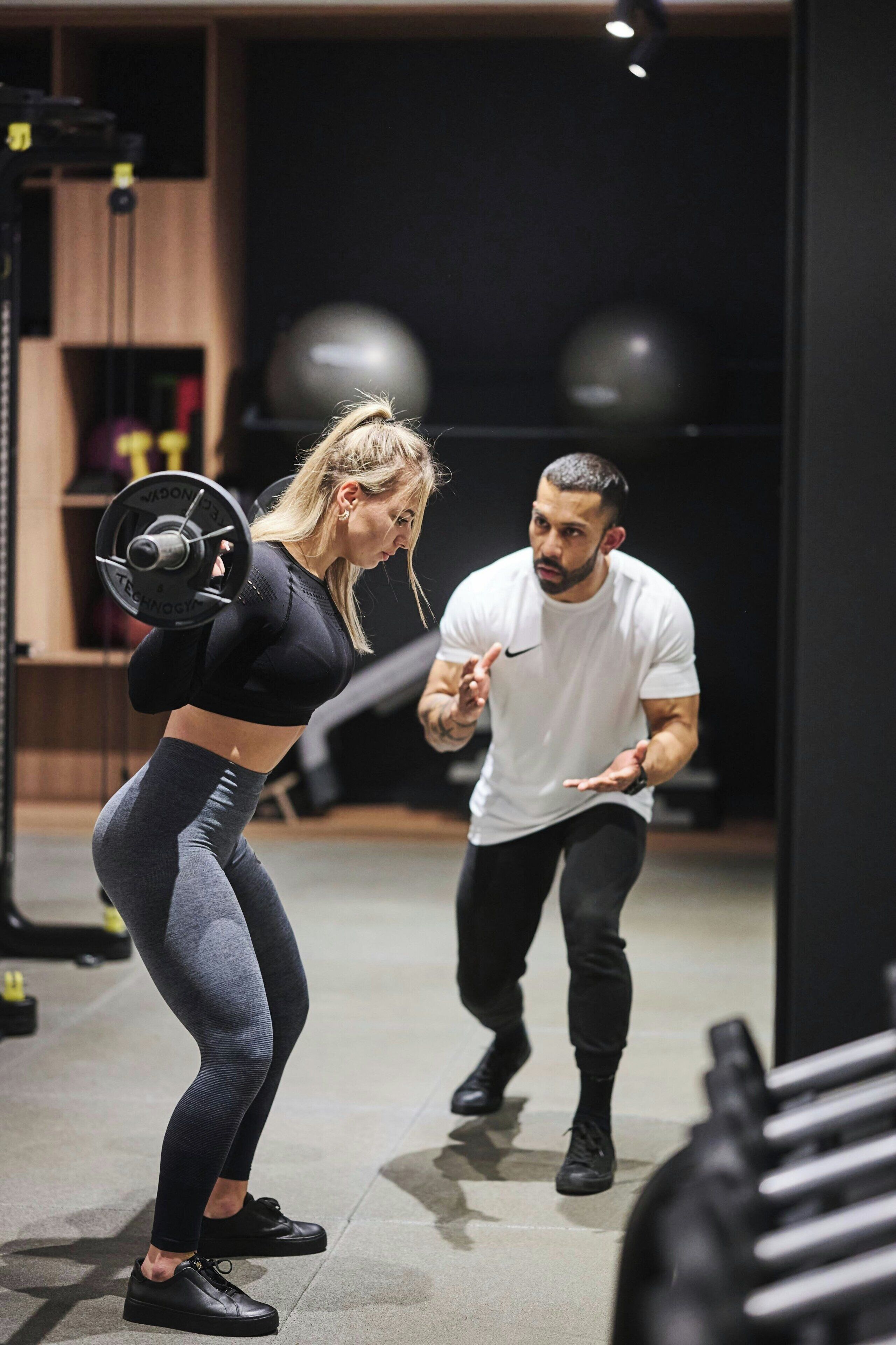 Un gimnasio con equipo de ejercicio, una persona levantando pesas y otra gesticulando.