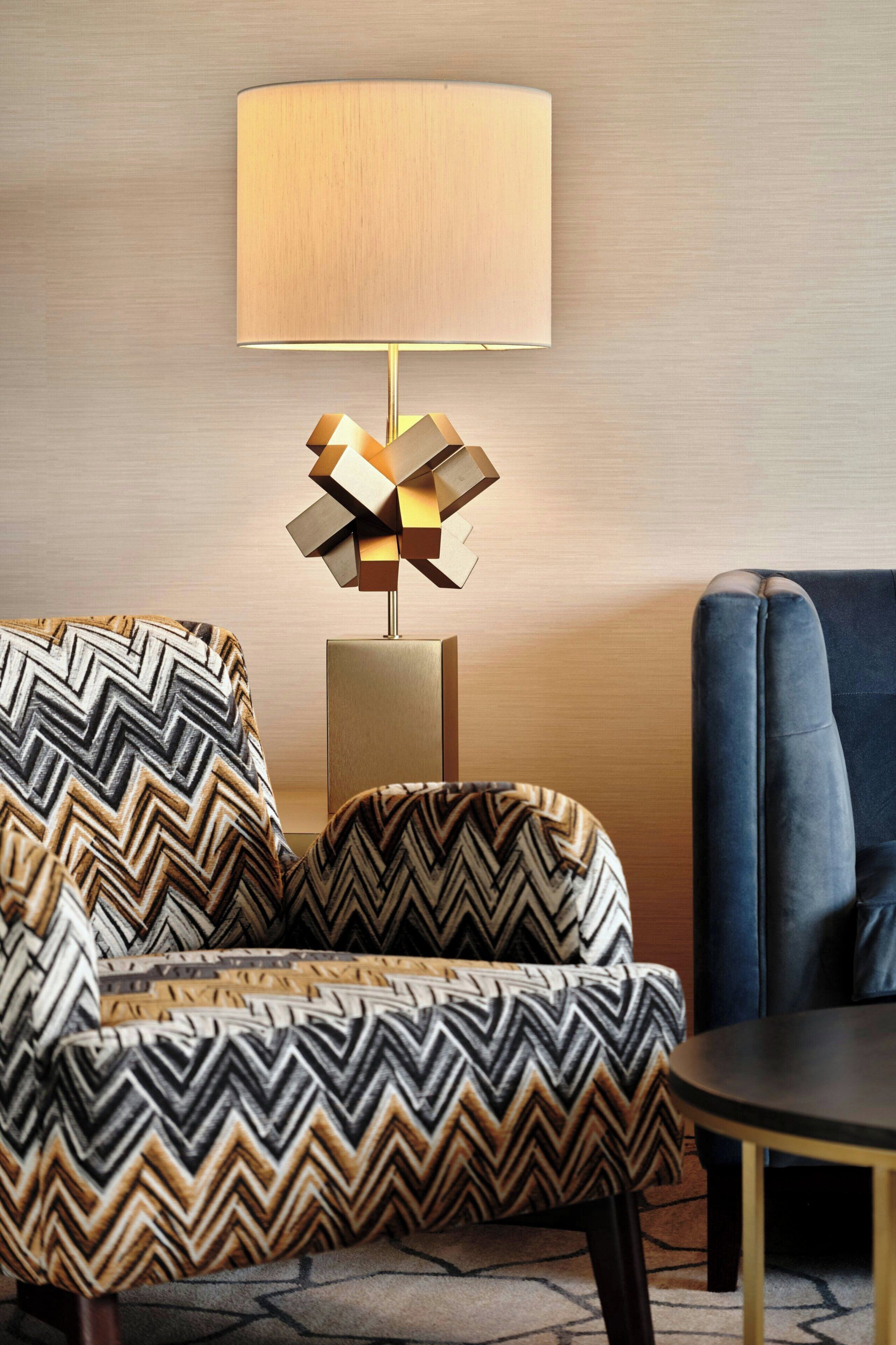 Una habitación moderna con un sillón estampado, un sofá azul y una lámpara de pie geométrica.