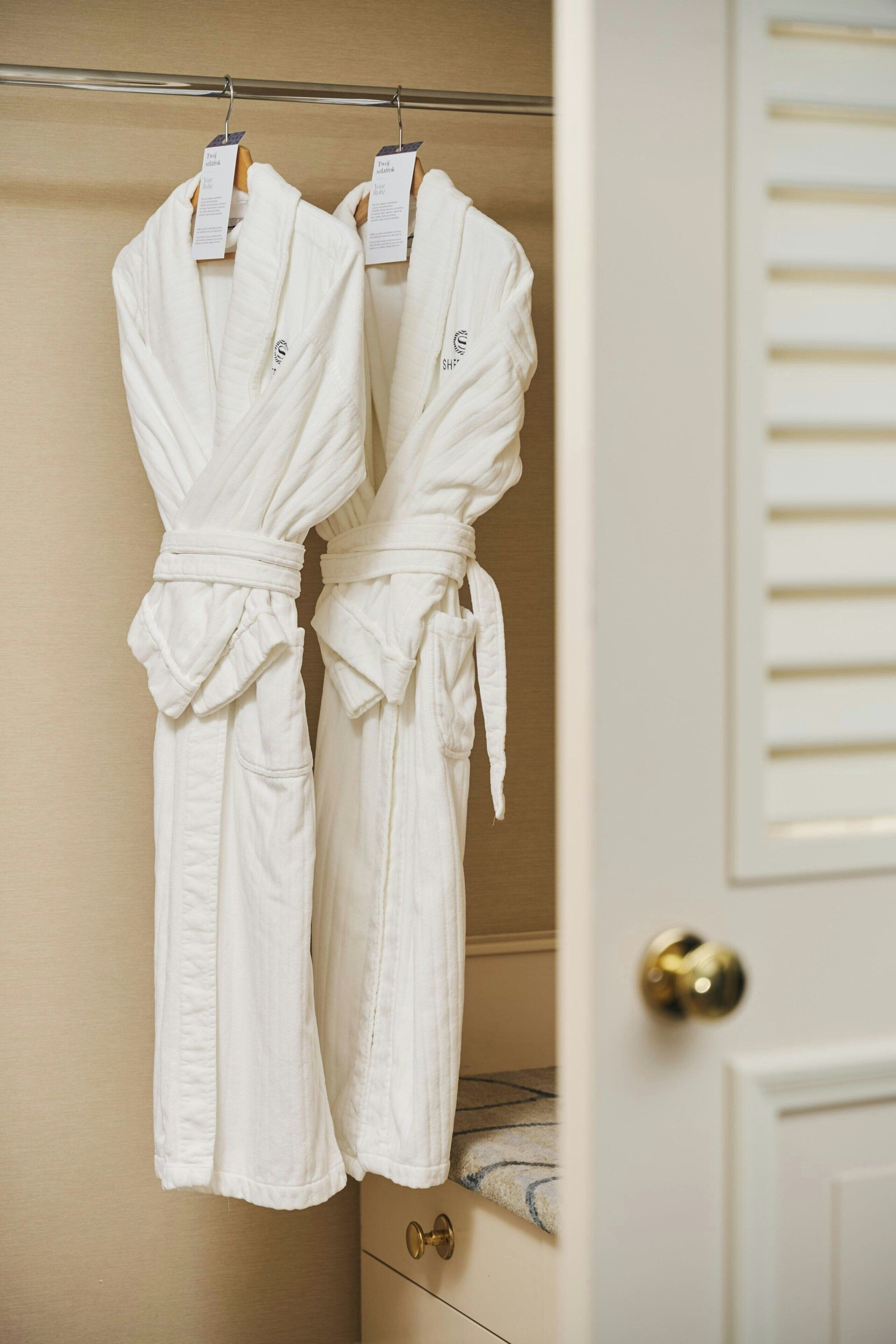 A closet with two white robes hanging on a rod.