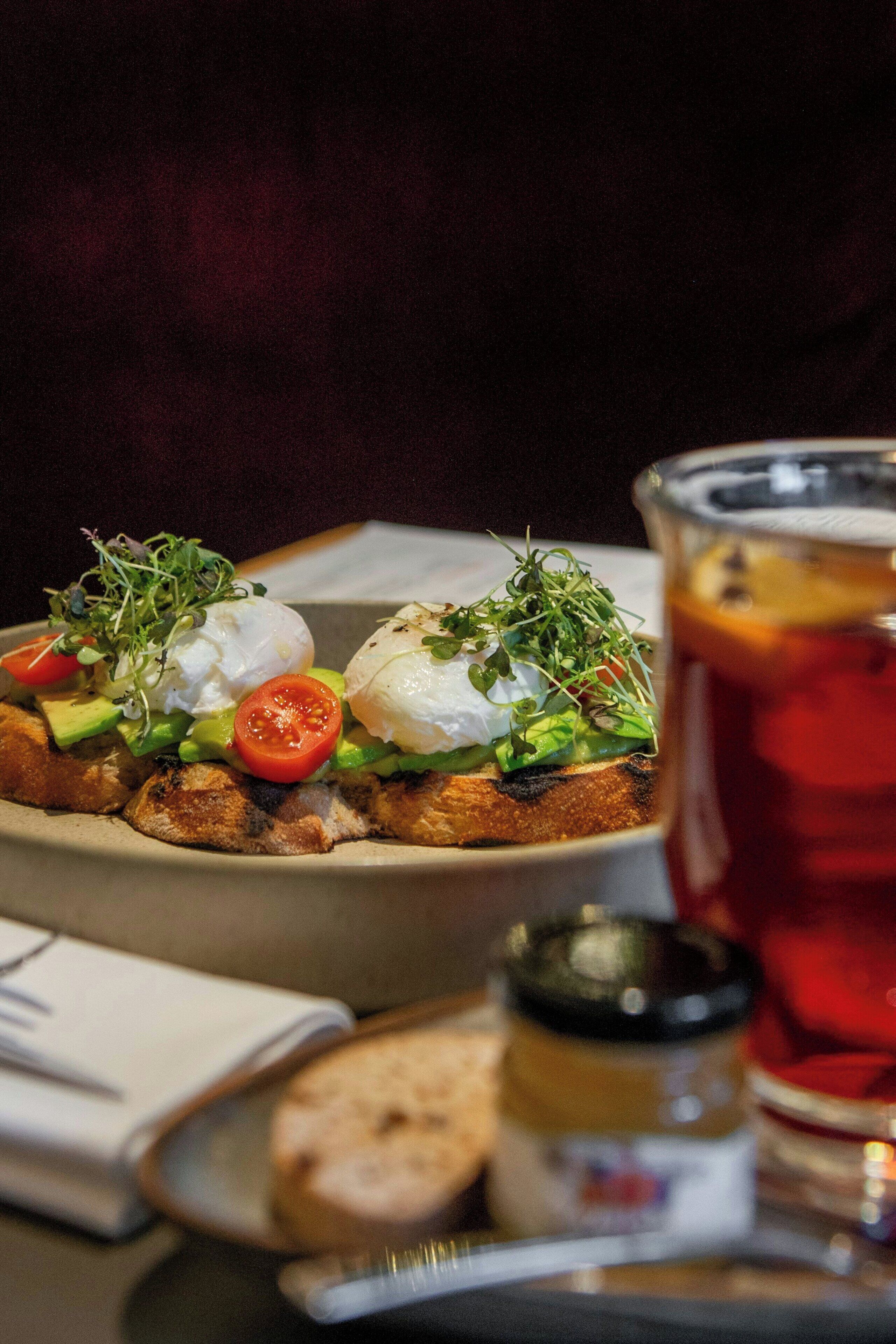 A plate of food with poached eggs, avocado, and tomatoes, and a glass of red beverage.