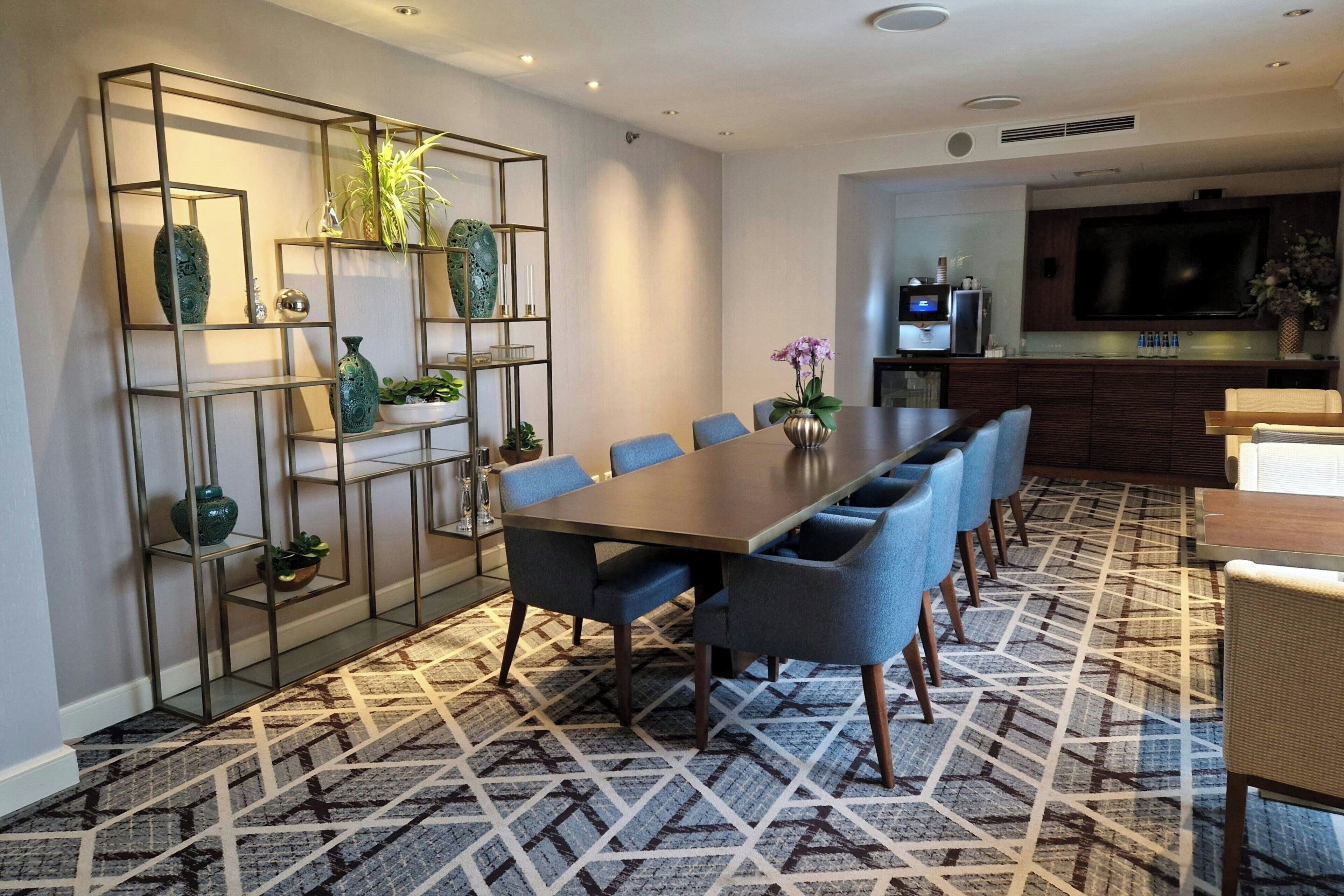 A modern dining area with a long table, blue chairs, and a patterned carpet.