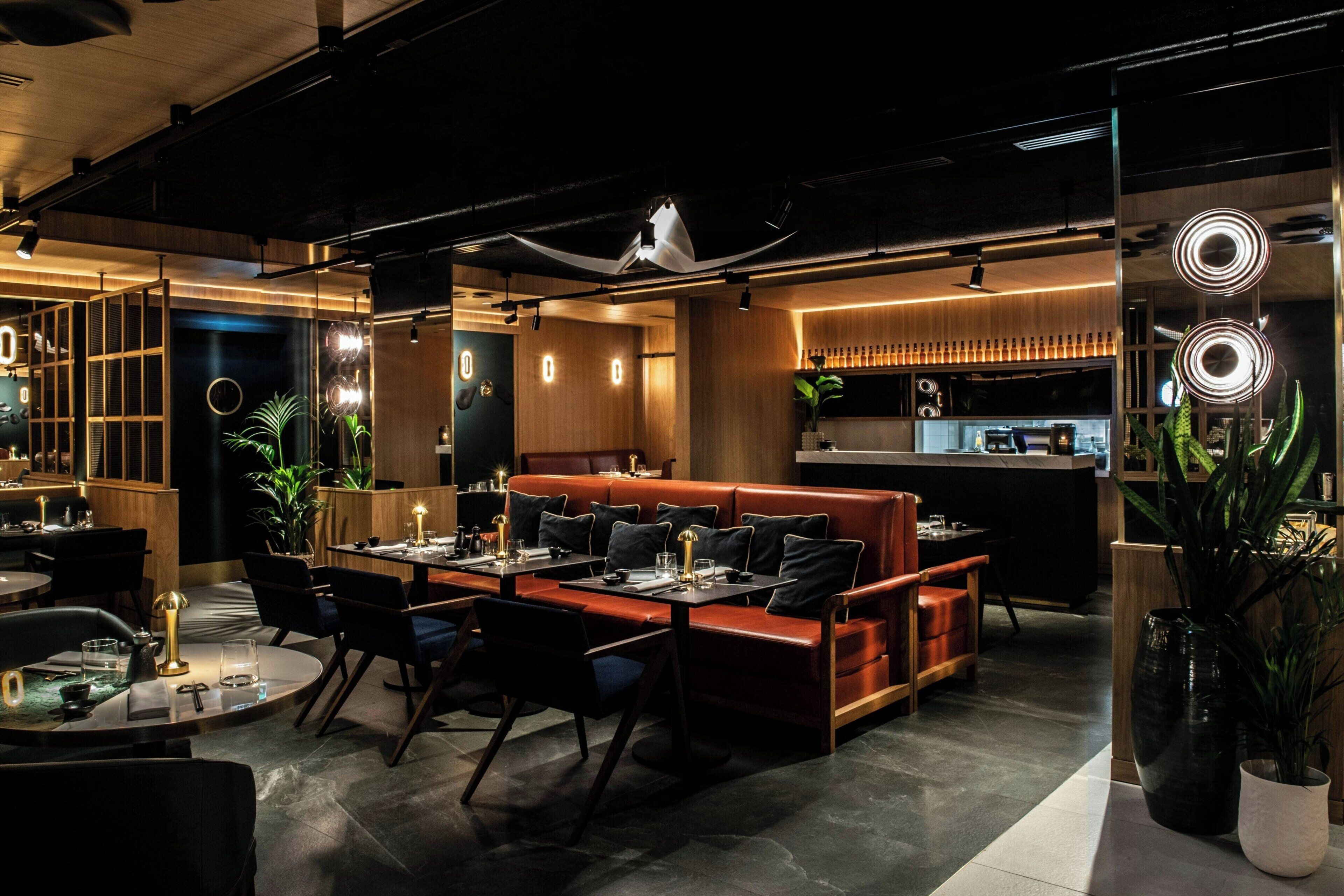 Un restaurante moderno con barra, mesas y una cocina visible al fondo.