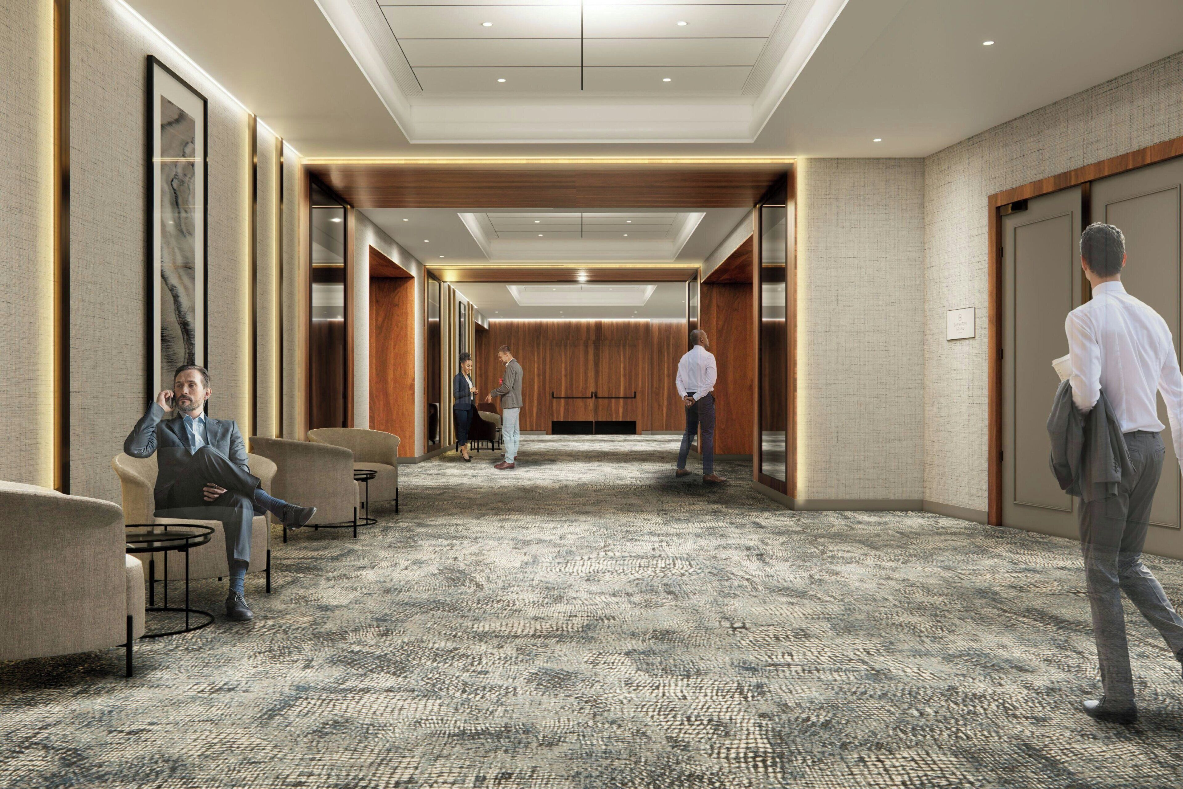 A modern hotel lobby with a carpeted floor, seating areas, and a wooden accent wall.