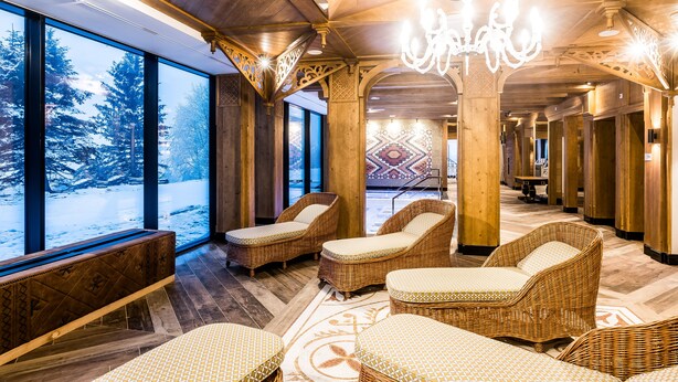 A spa area with wicker loungers, large windows with a snowy view, and a chandelier.
