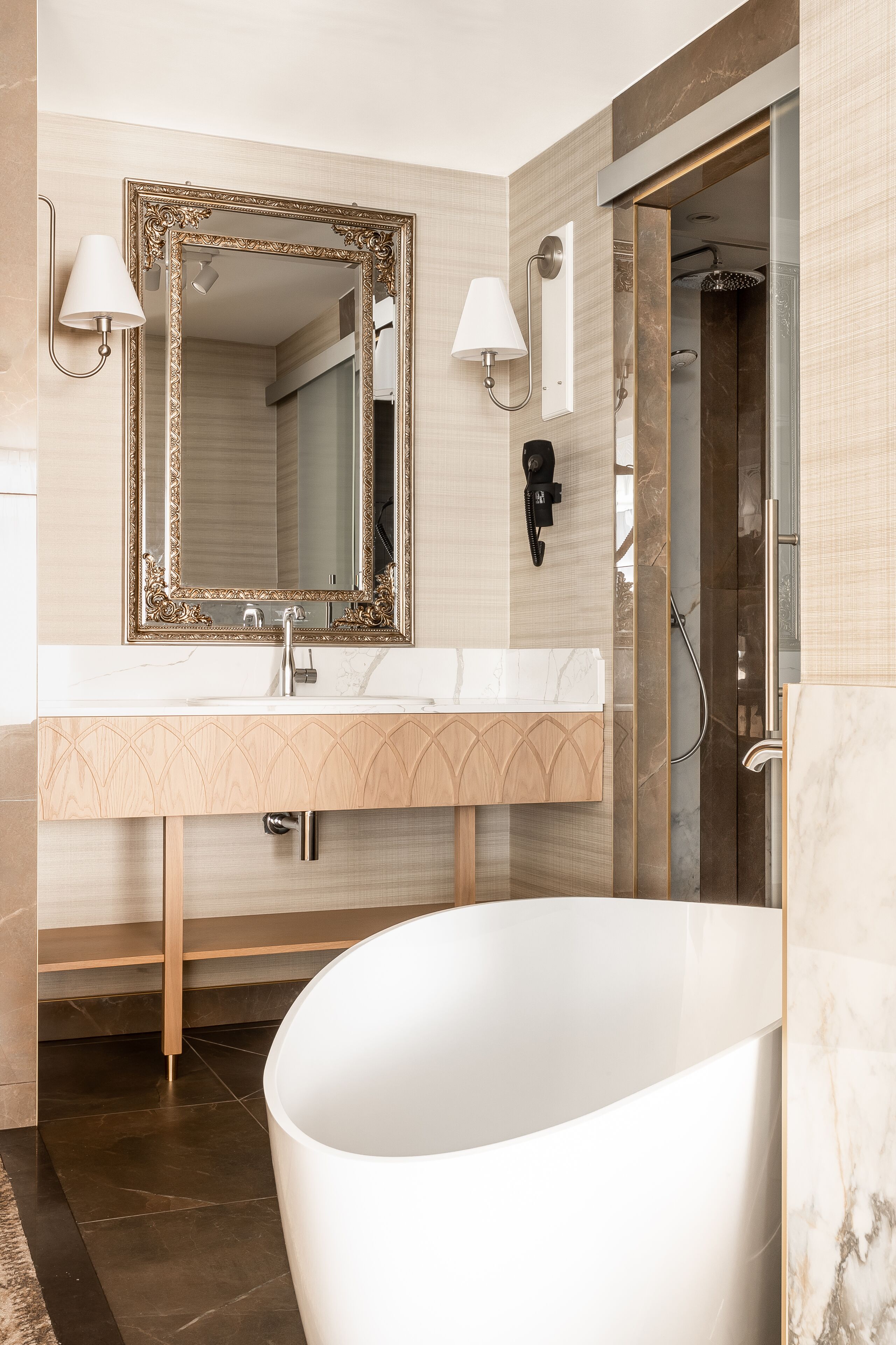 Un baño moderno con una bañera independiente, un espejo grande con un marco ornamentado y un tocador con encimera de mármol.