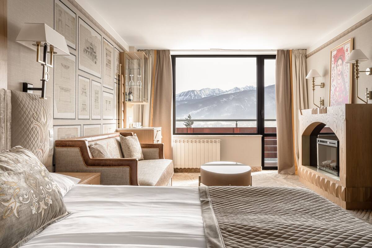 A hotel room with a large bed, a seating area with a view of mountains, a fireplace, and framed pictures on the wall.