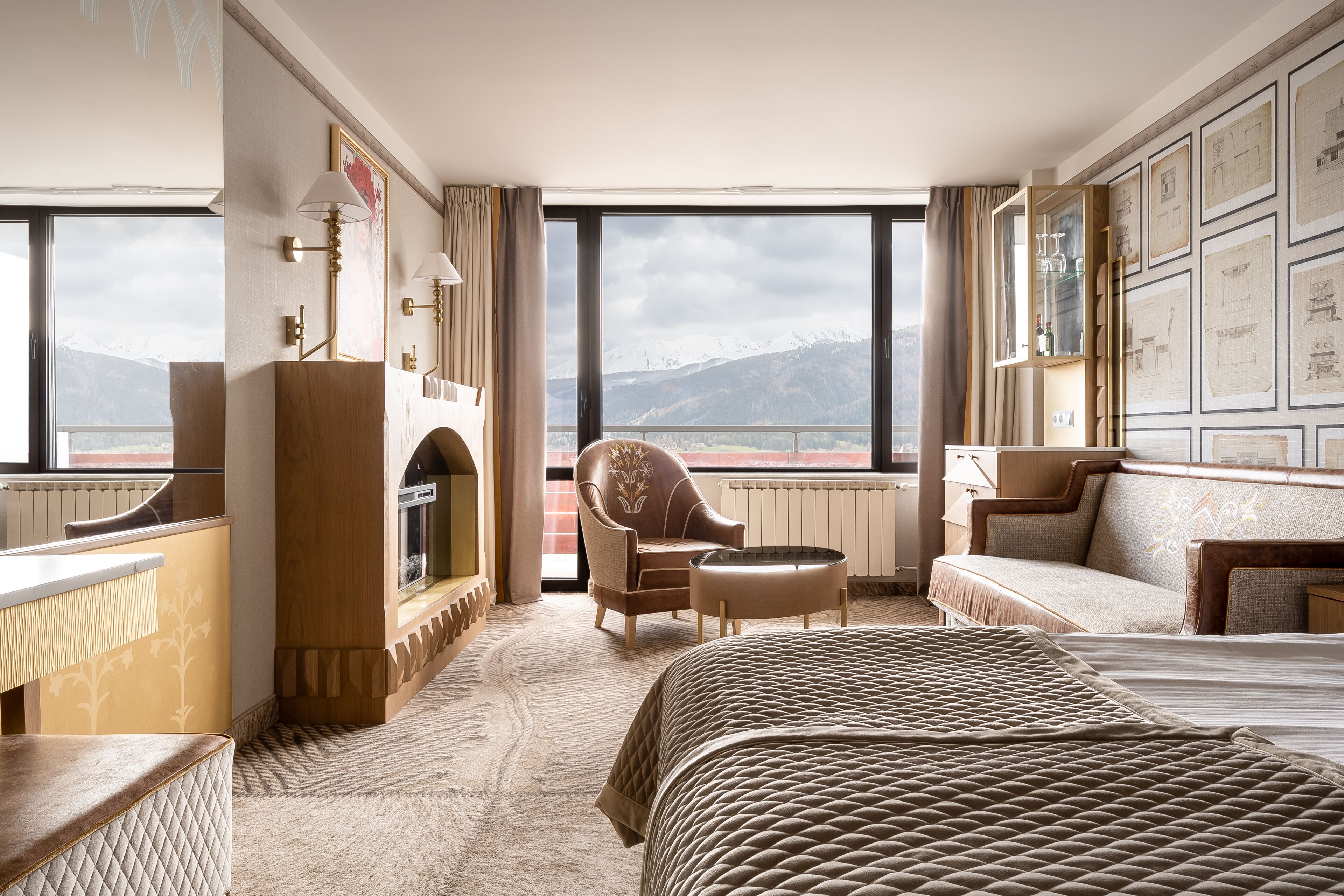 Une chambre d’hôtel équipée d’un lit, d’un canapé, d’un fauteuil, d’une cheminée et de grandes fenêtres donnant sur une vue imprenable sur les montagnes.