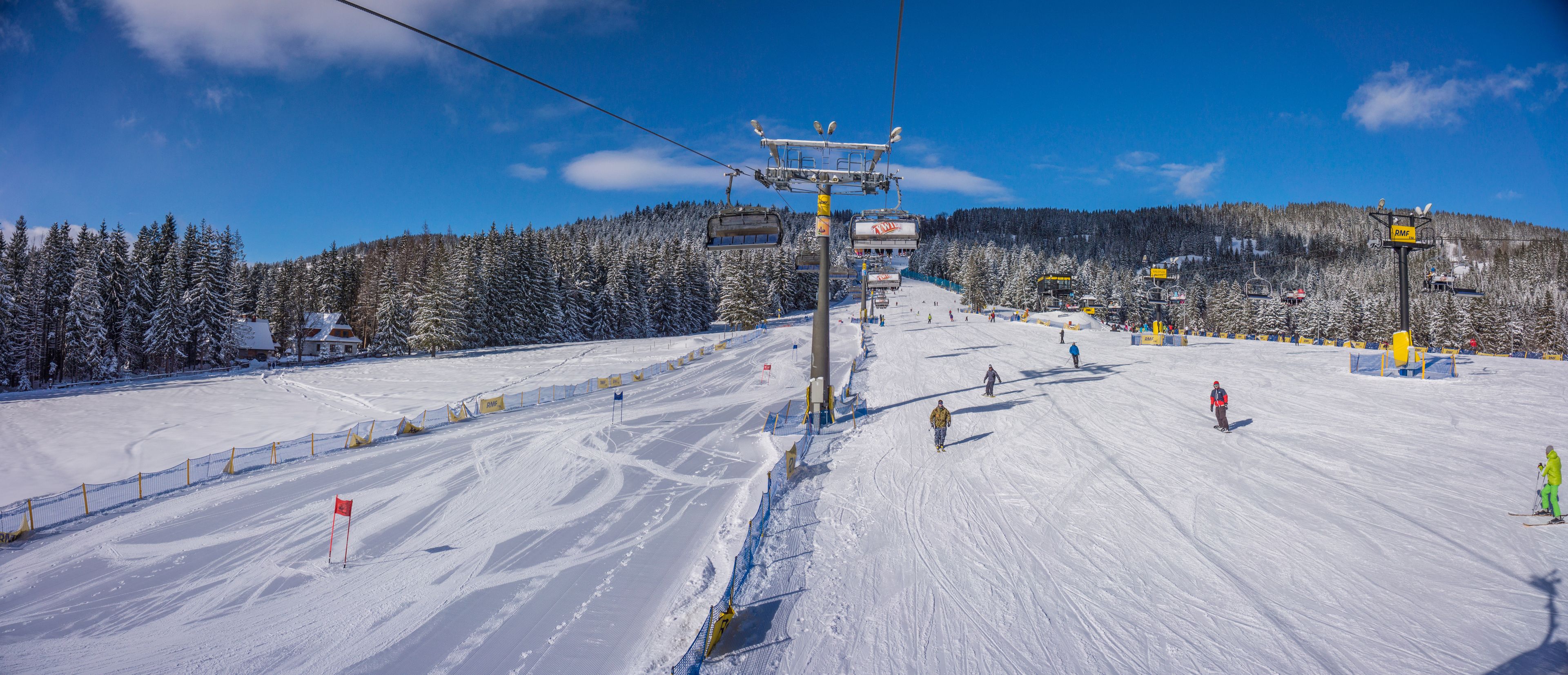 A ski slope with a chairlift, snow-covered trees, and a clear sky.