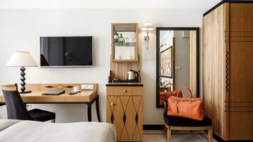 A hotel room with a bed, a desk with a lamp, a wooden cabinet, a mirror, and a wardrobe.